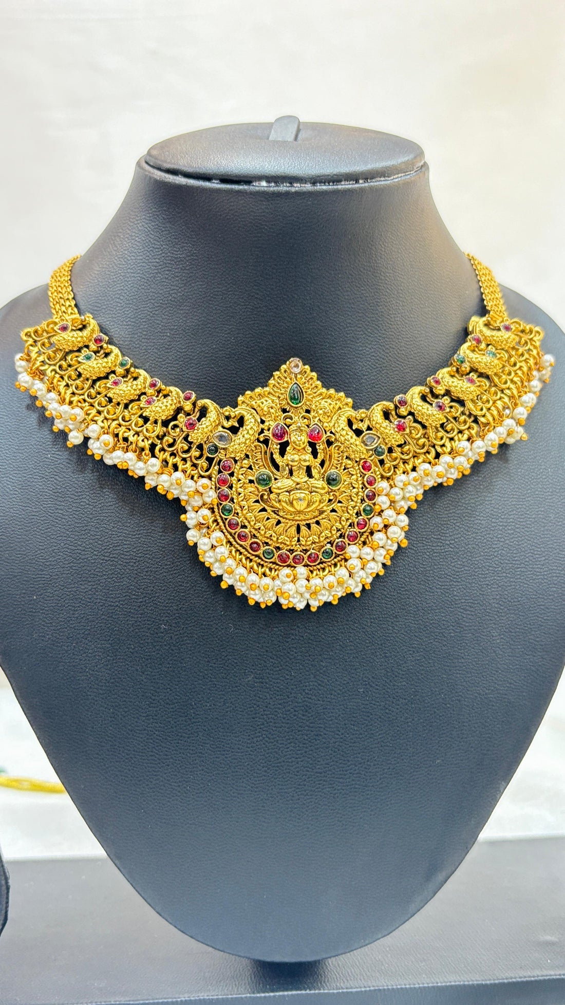 Gold necklace and earrings set on a black mannequin bust with a white background