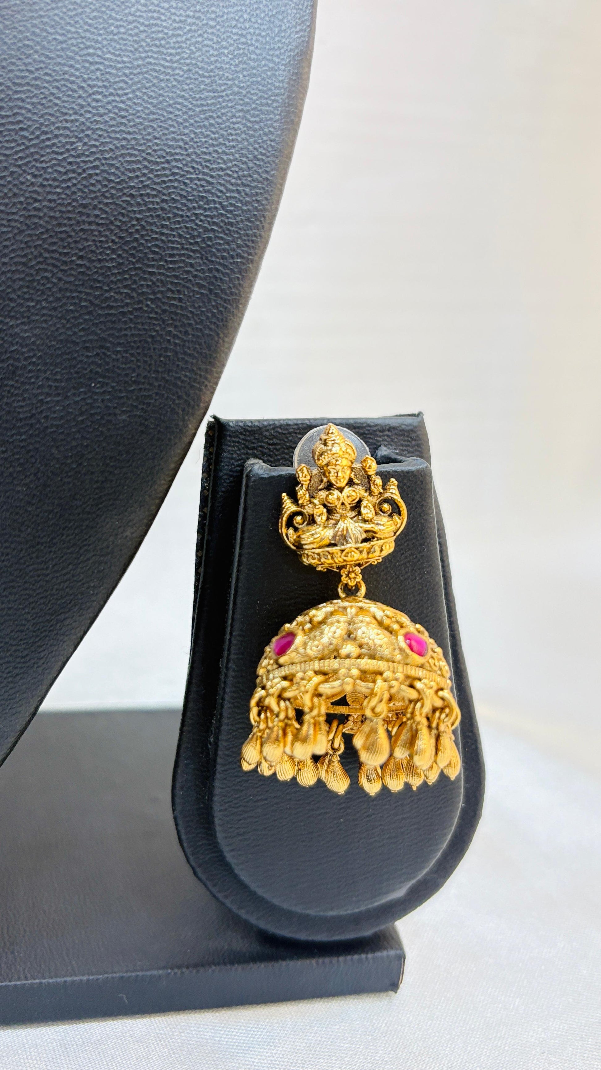 Gold earrings with pink stones on a black stand against a white background