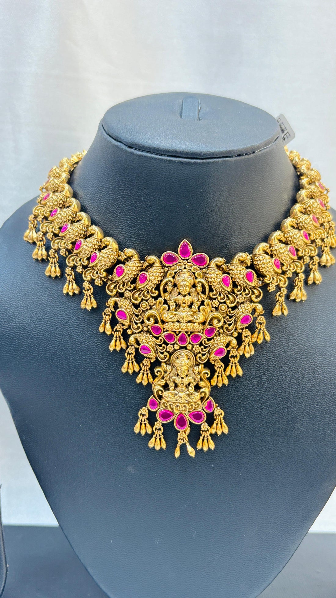 Gold necklace and earrings set on a black stand with a white background