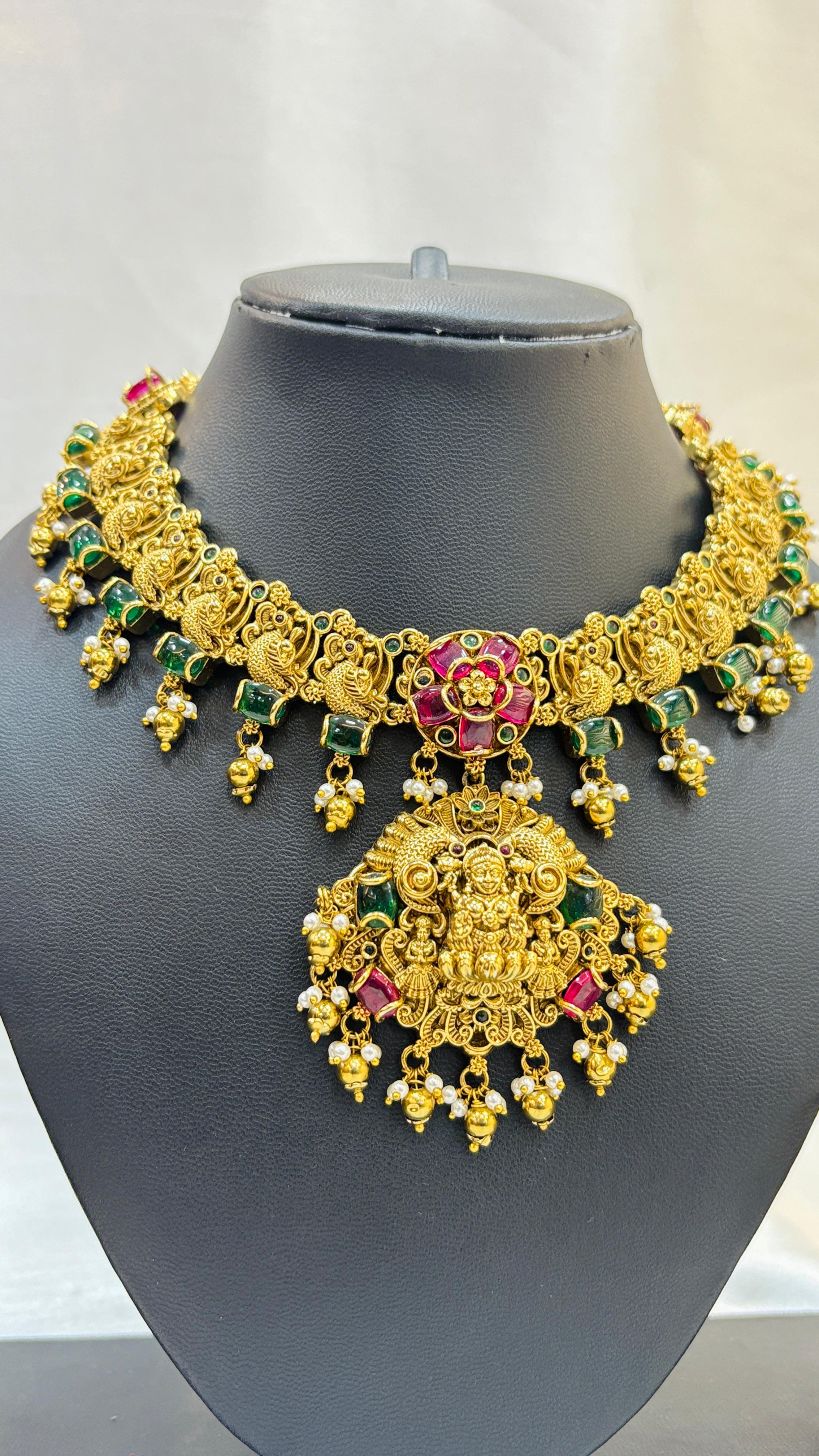Gold necklace with green and red stones on a black mannequin