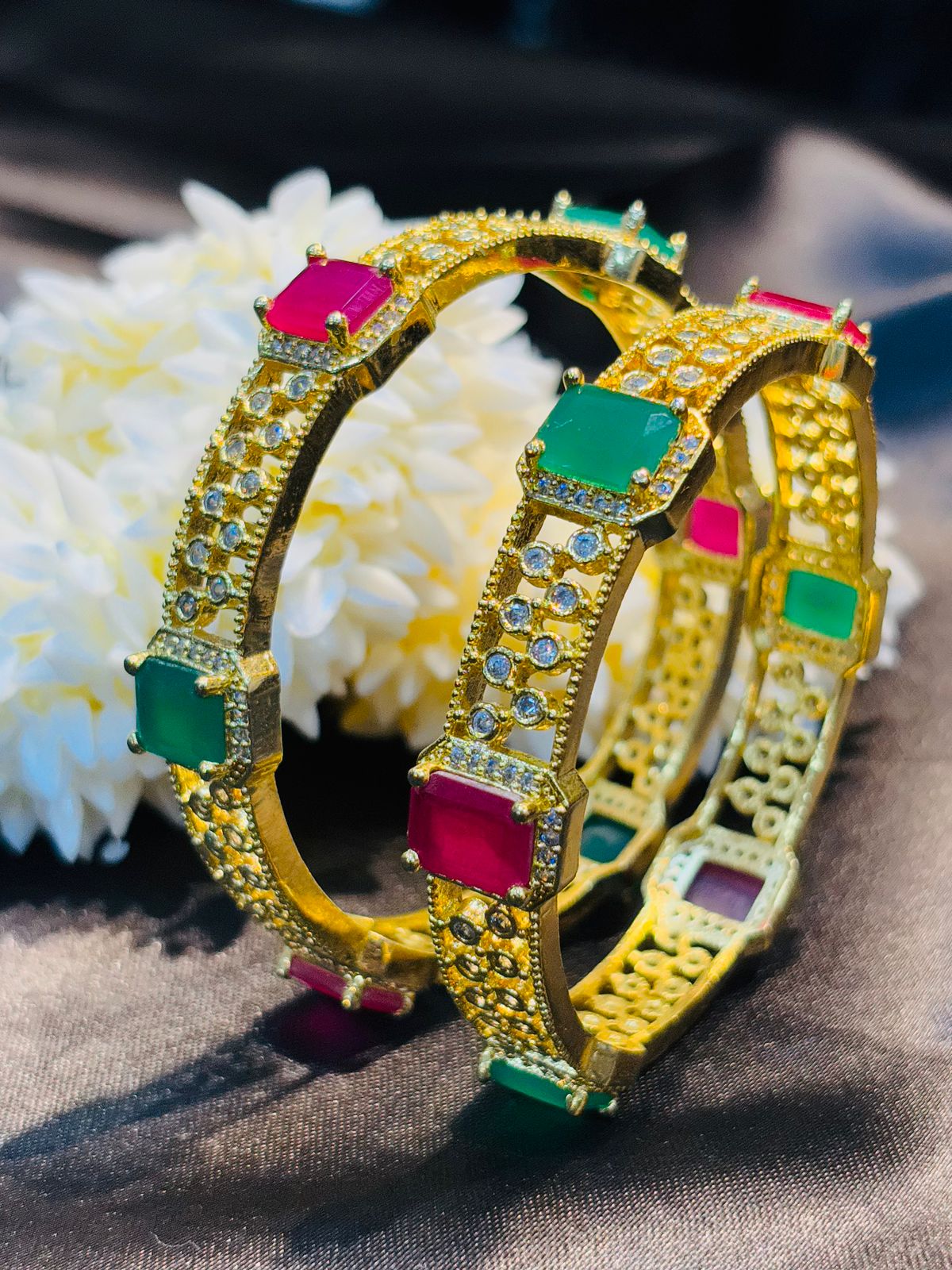 Gold bangles with colorful gemstones on a textured surface