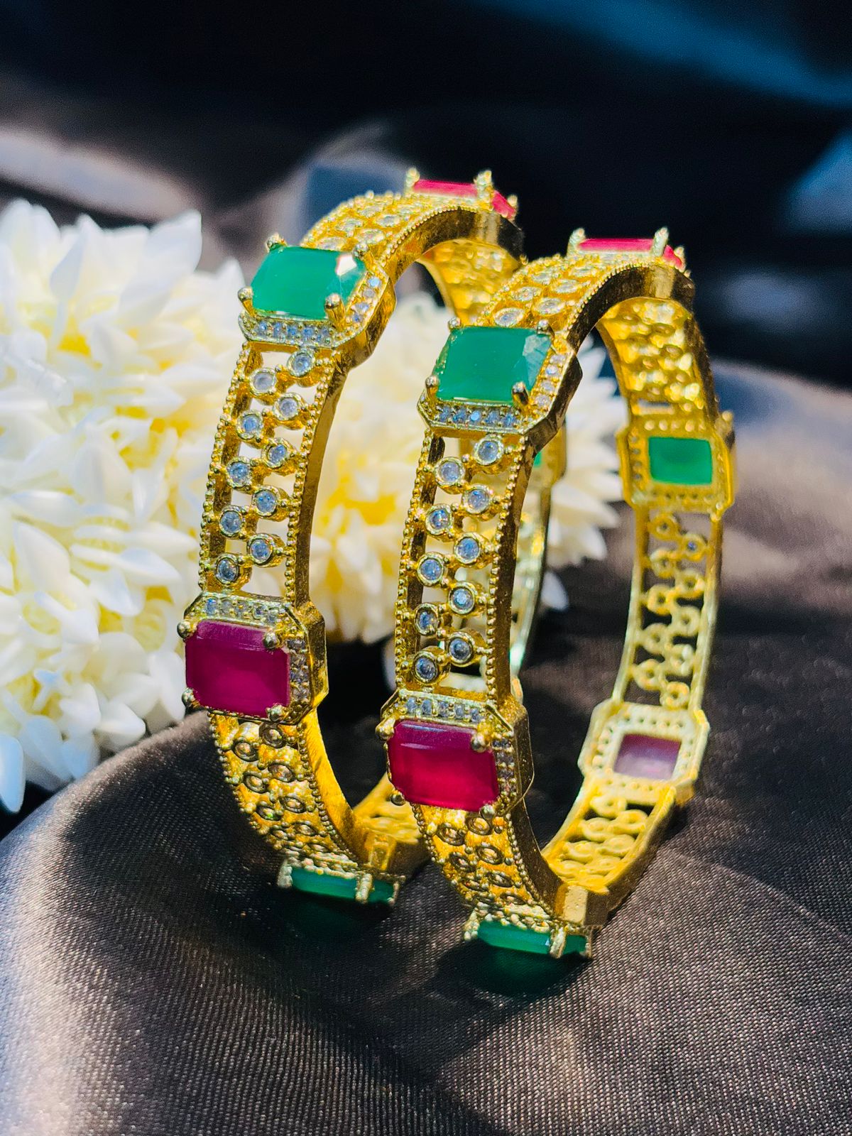Gold bangles with gemstones on a dark fabric background