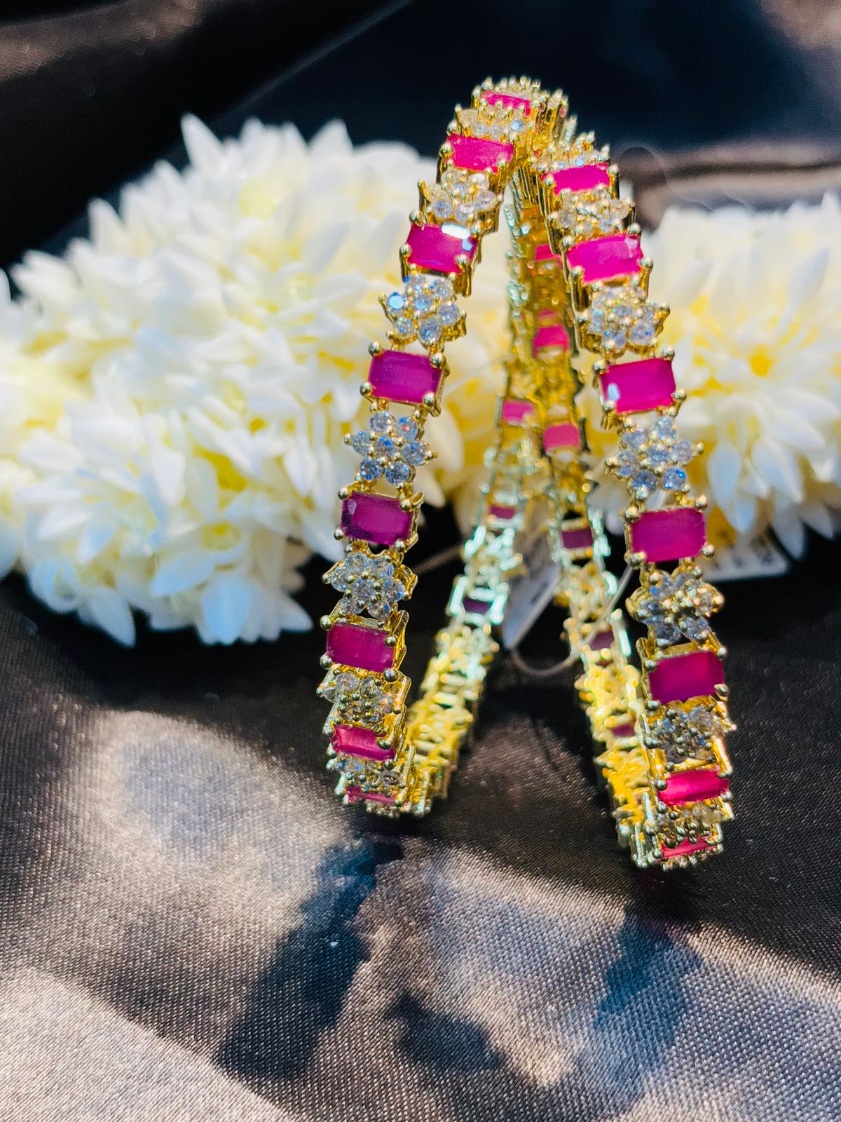 Gold hoop earrings with pink gemstones on a dark surface with white flowers.