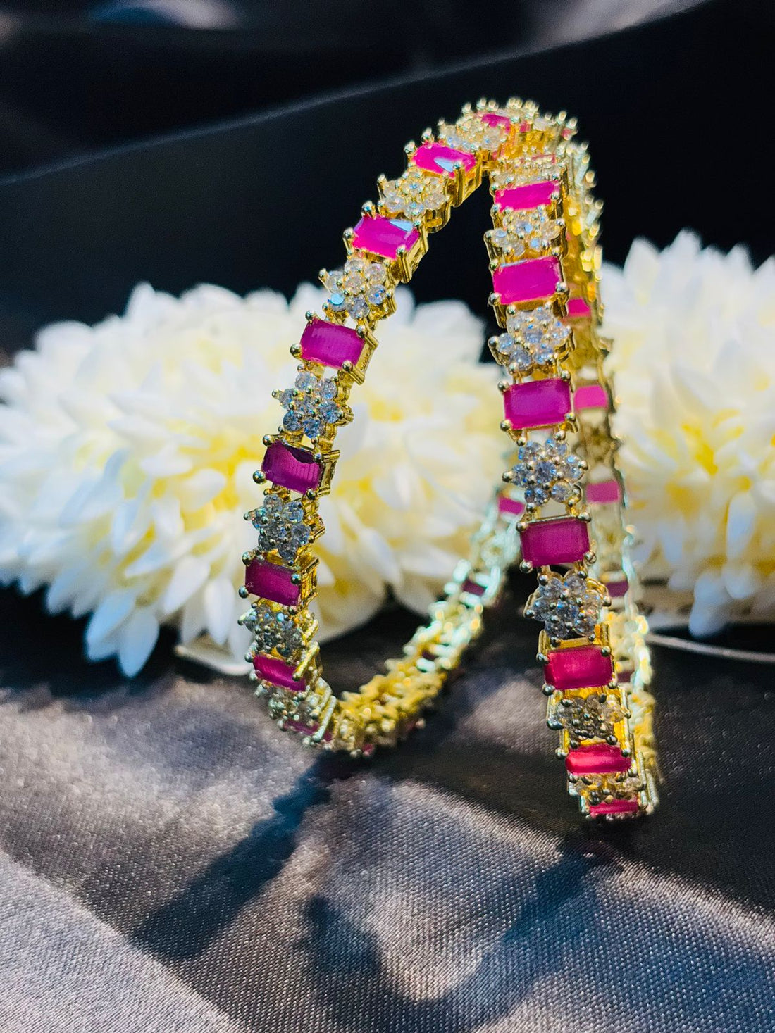 Gold hoop earrings with pink gemstones on a dark surface with white flowers.