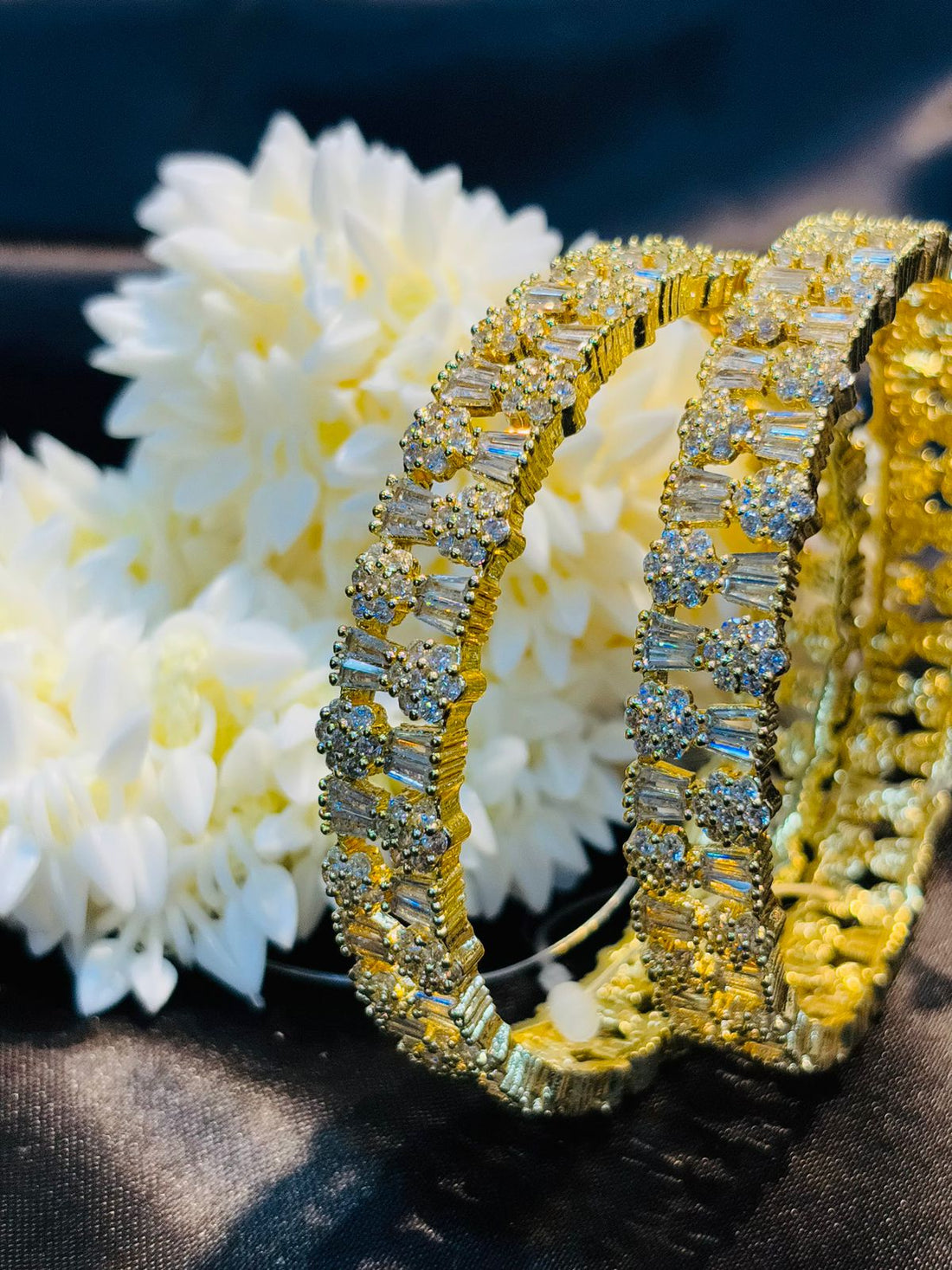 Gold and diamond bracelet on a dark surface with white flowers