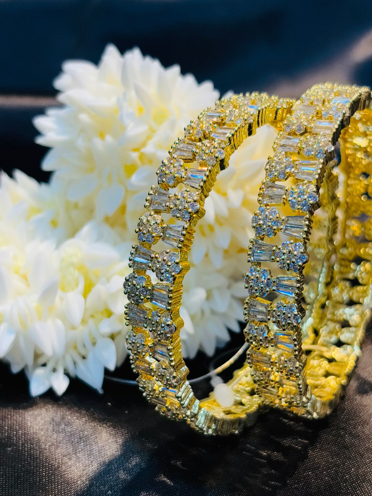 Gold and diamond bracelet on a dark surface with white flowers in the background