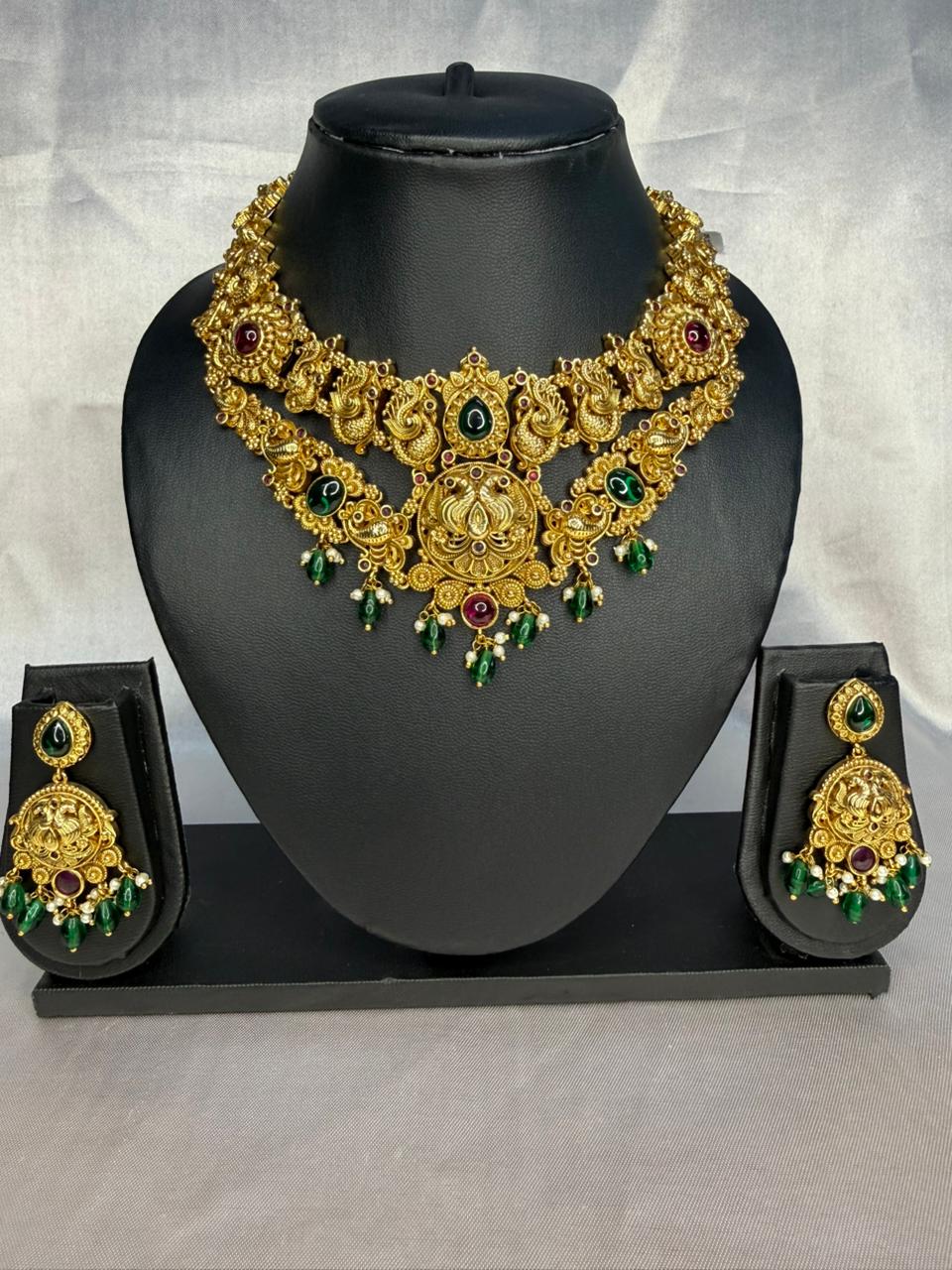 Gold necklace with green and red stones on a black mannequin