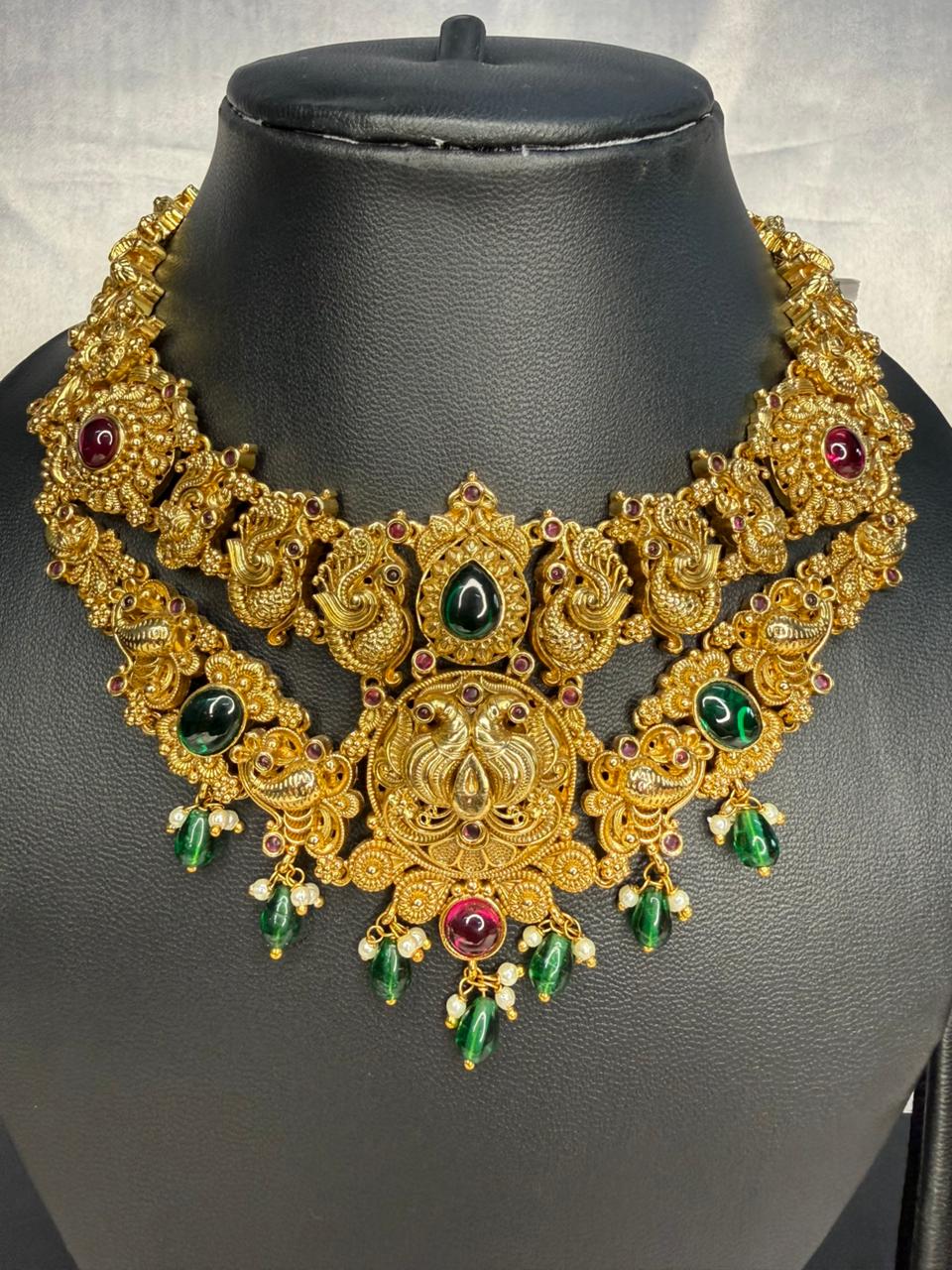 Gold necklace with green and red stones on a black mannequin