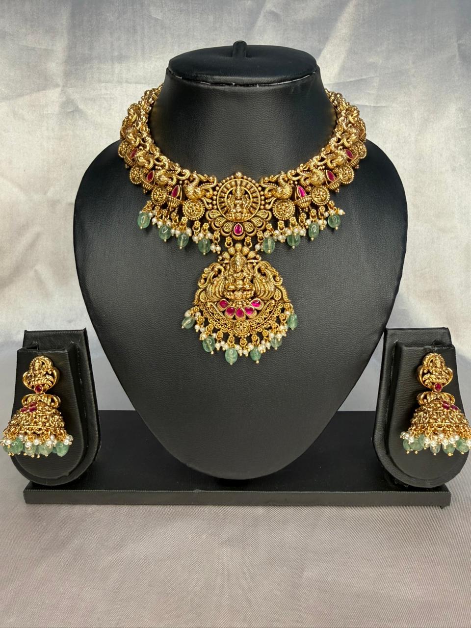 Gold necklace with green and red stones on a black mannequin bust against a gray background