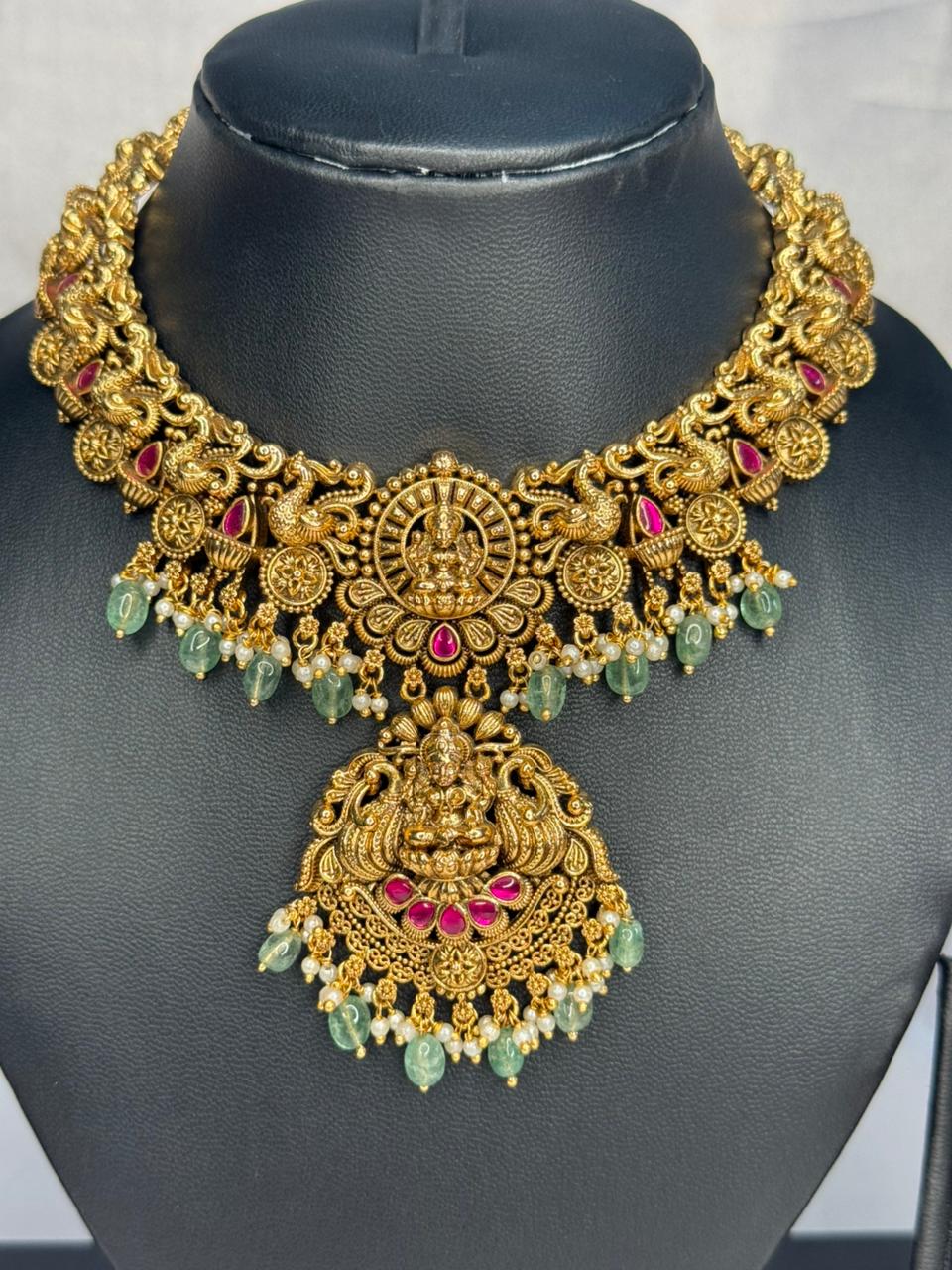 Gold necklace with red and green stones on a black mannequin
