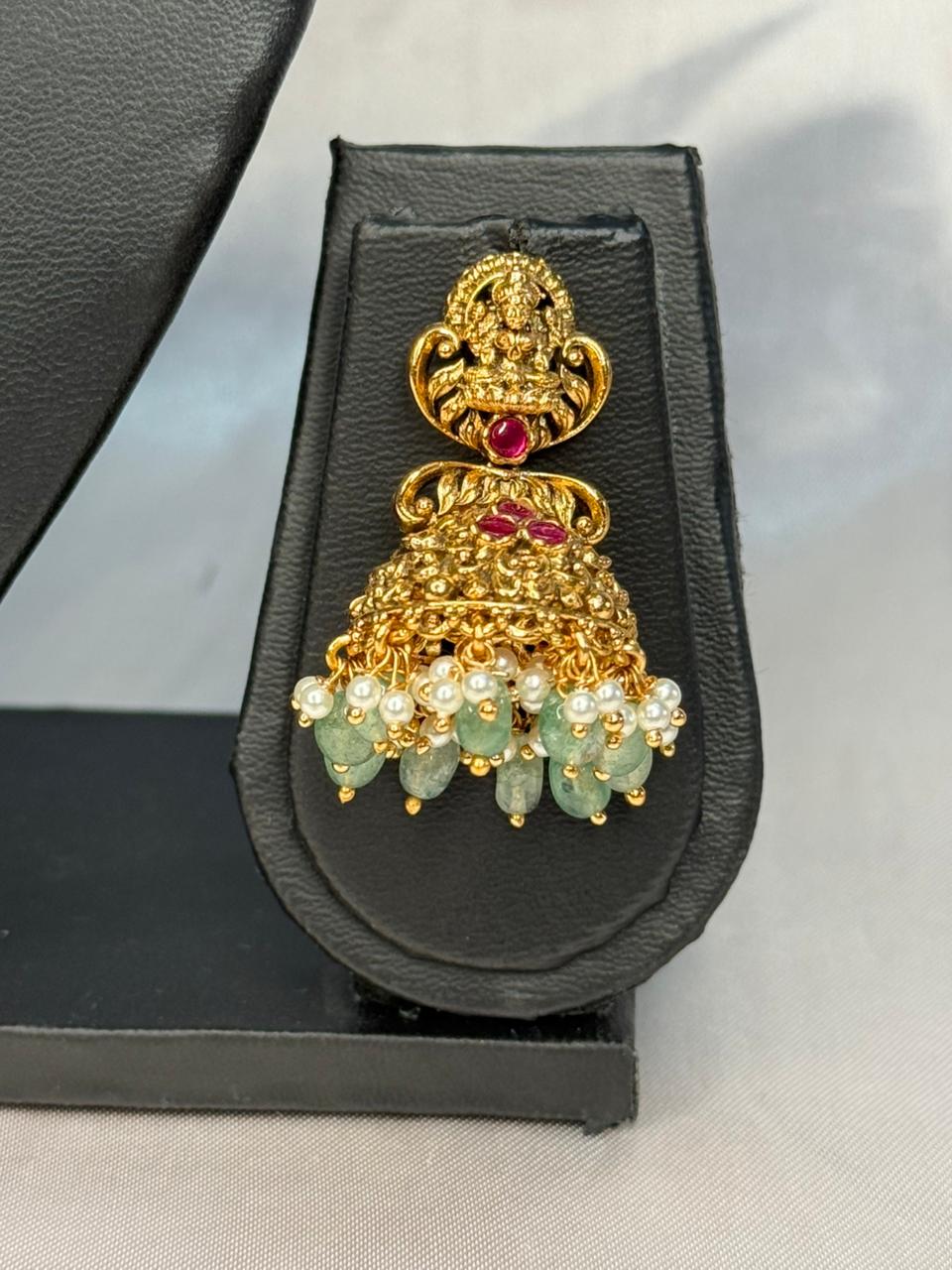 Gold jhumka earring with red gemstone on a black stand