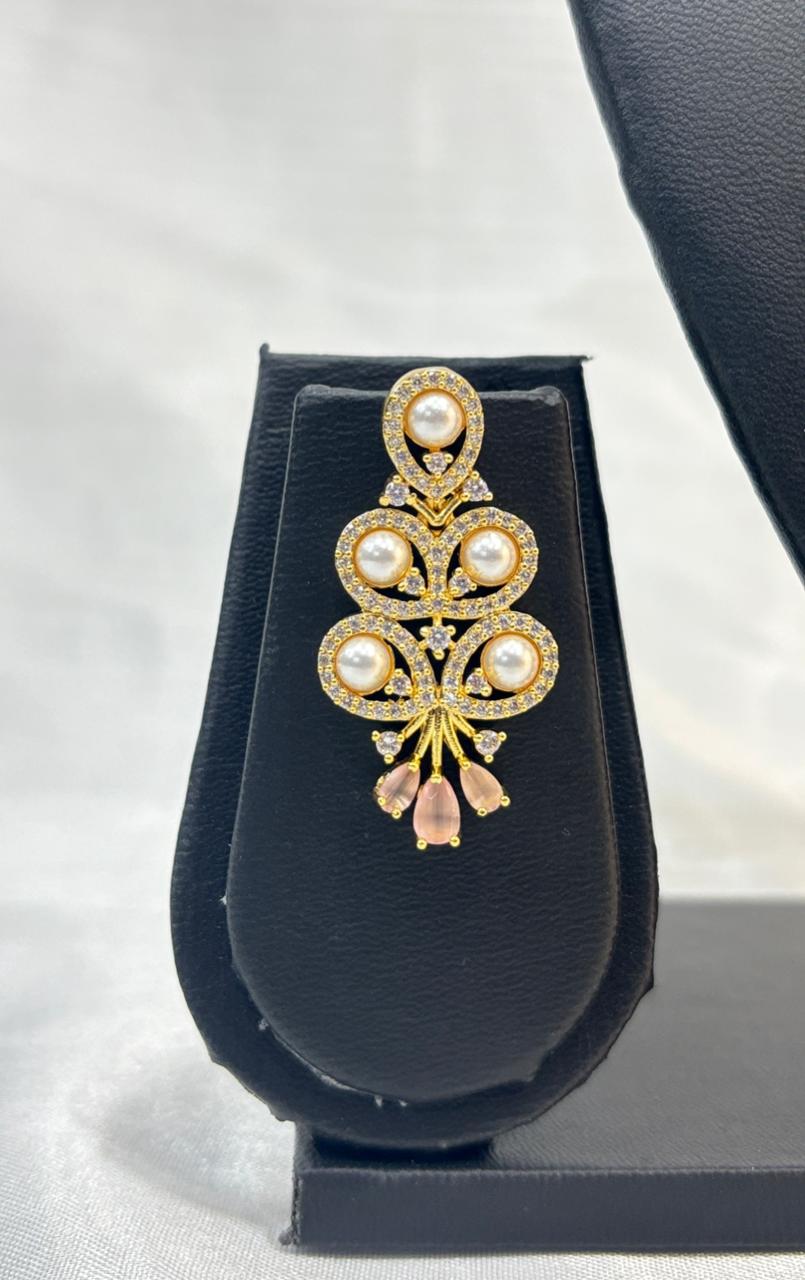 Decorative brooch with pearls and gemstones on a black stand against a white background