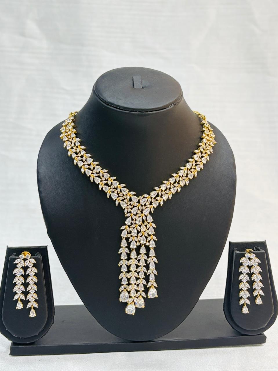 Gold and diamond necklace set on a black mannequin with matching earrings in display cases.