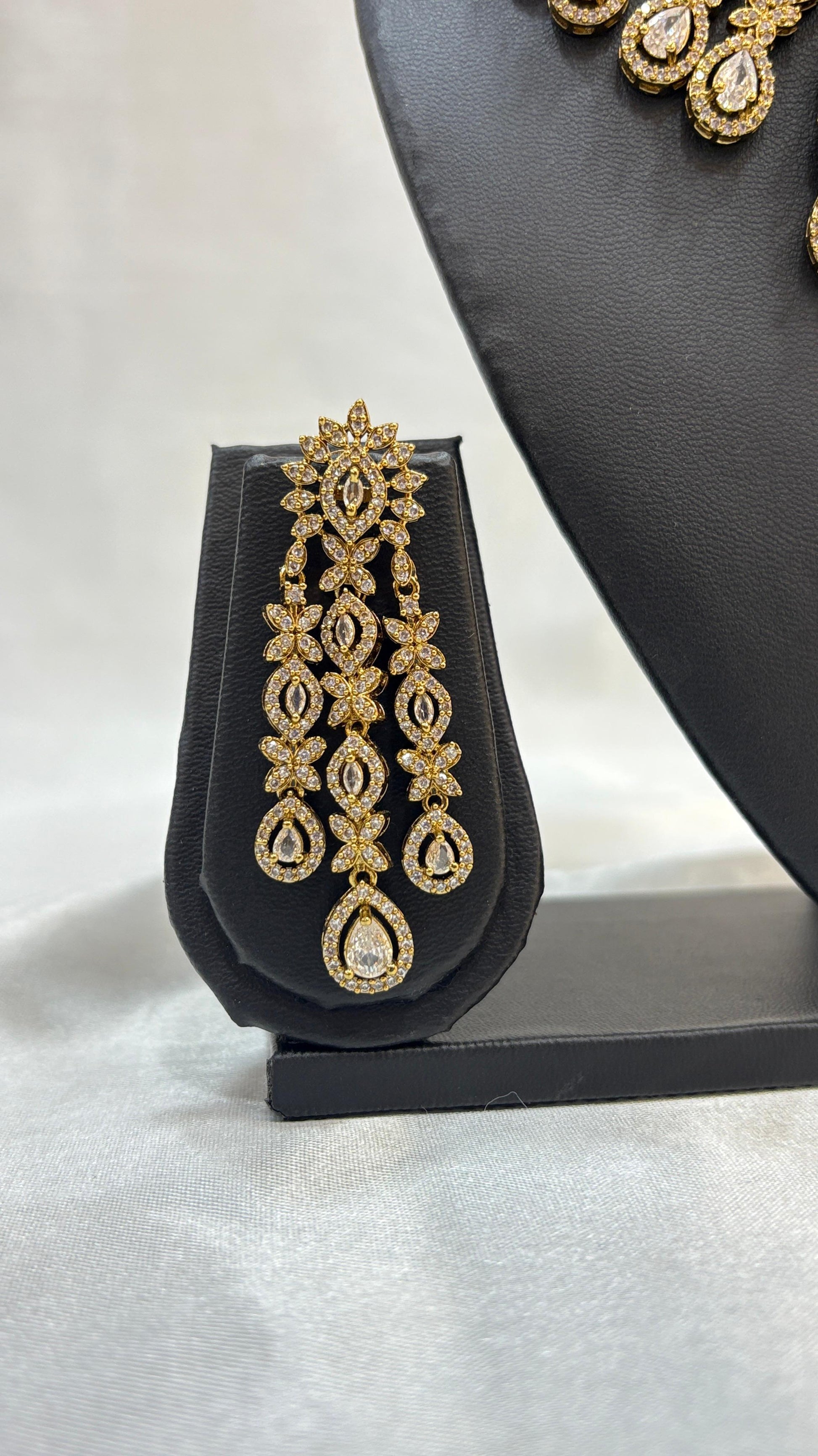 Gold earrings on a black earring stand with a gray background