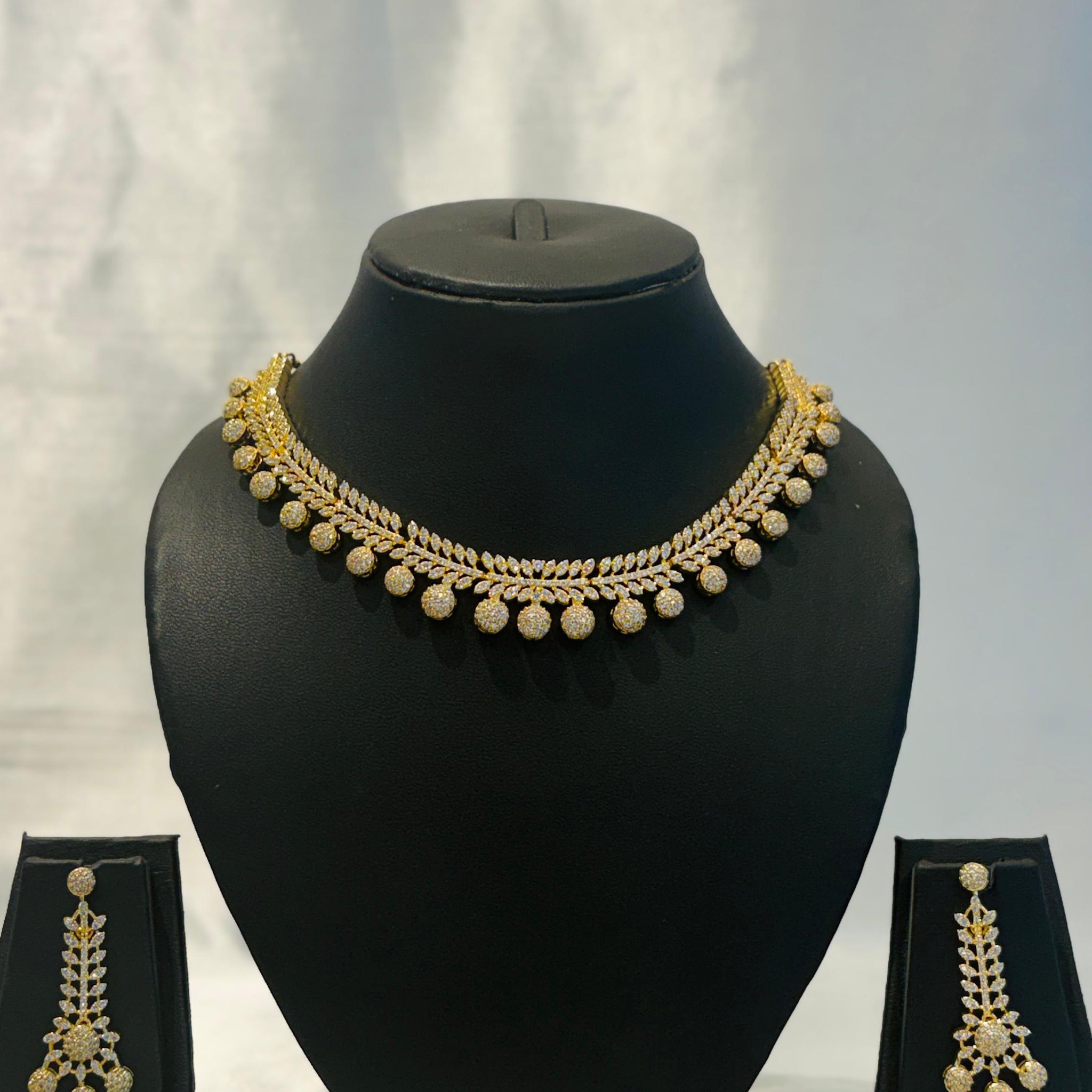 Gold necklace and earrings set on a black mannequin bust against a white background