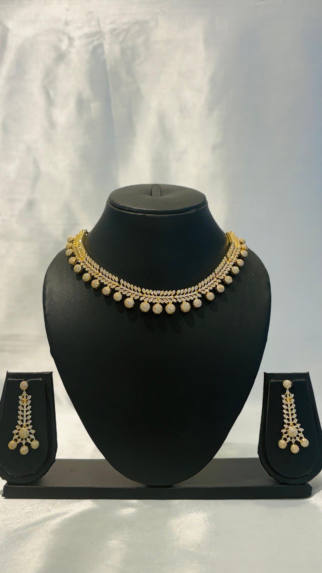 Gold necklace and earrings set on a black mannequin bust against a white background