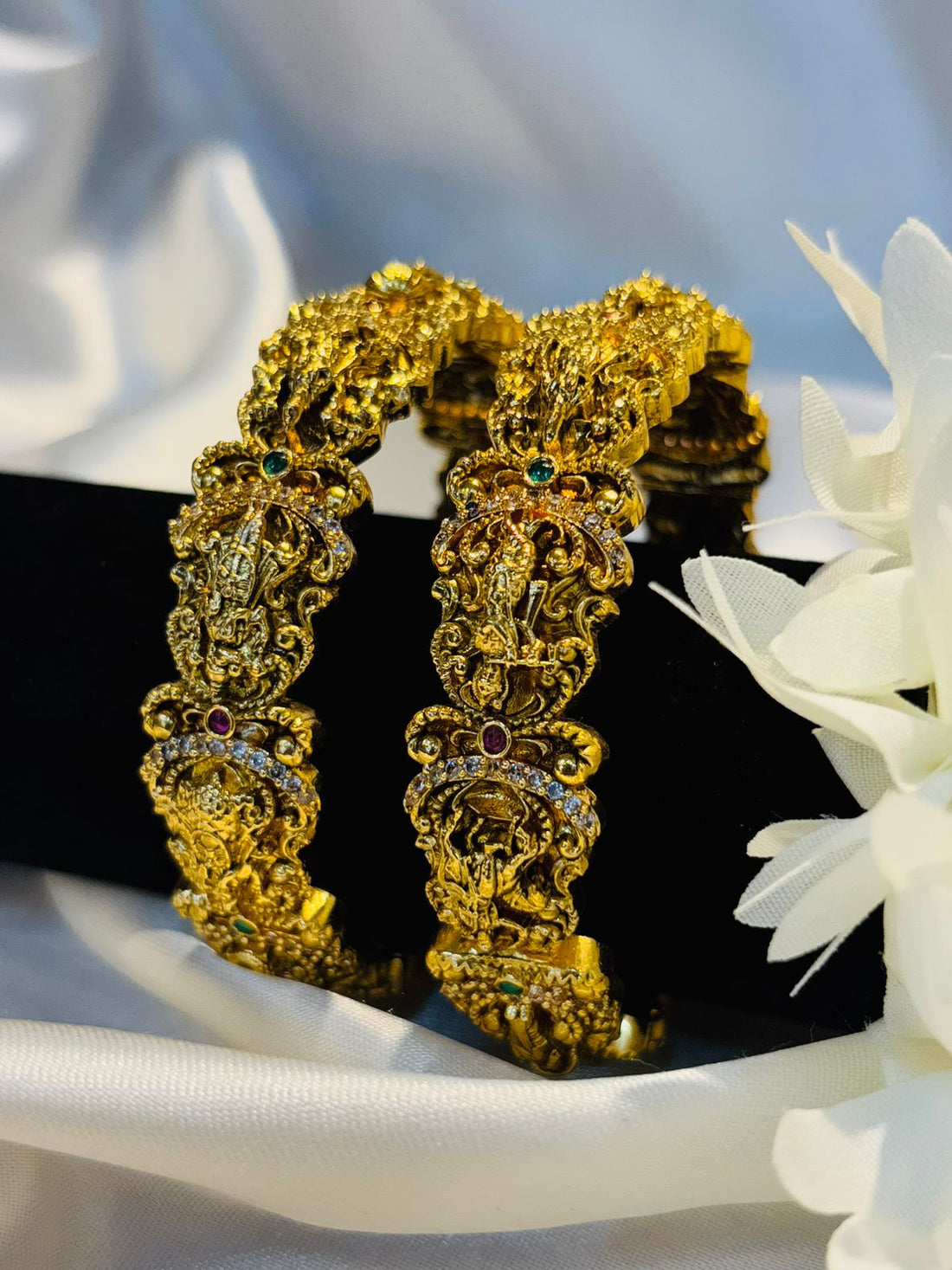 Gold earrings with intricate designs on a white surface with flowers.