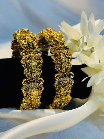 Gold earrings with intricate designs on a white surface with flowers.