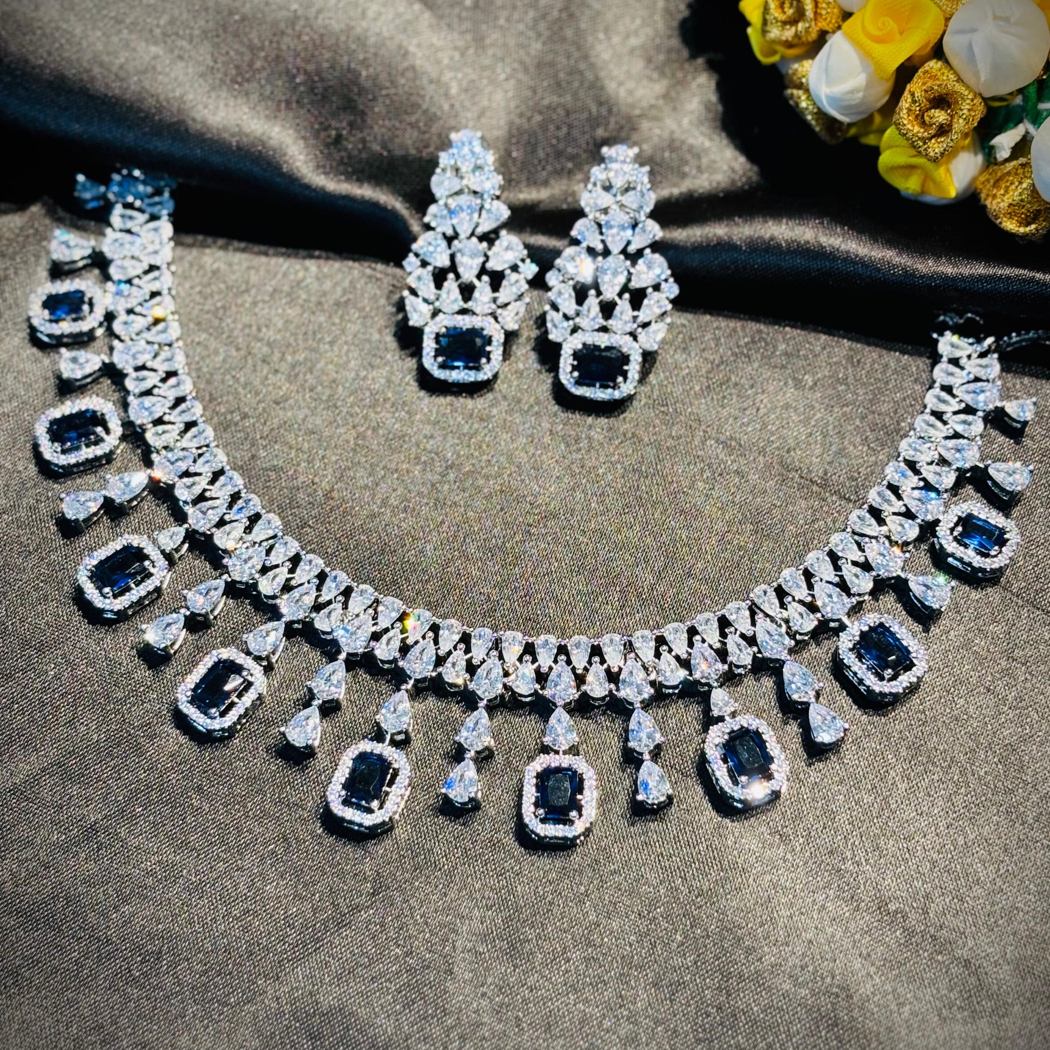 Diamond necklace and earrings on a dark fabric background with flowers.