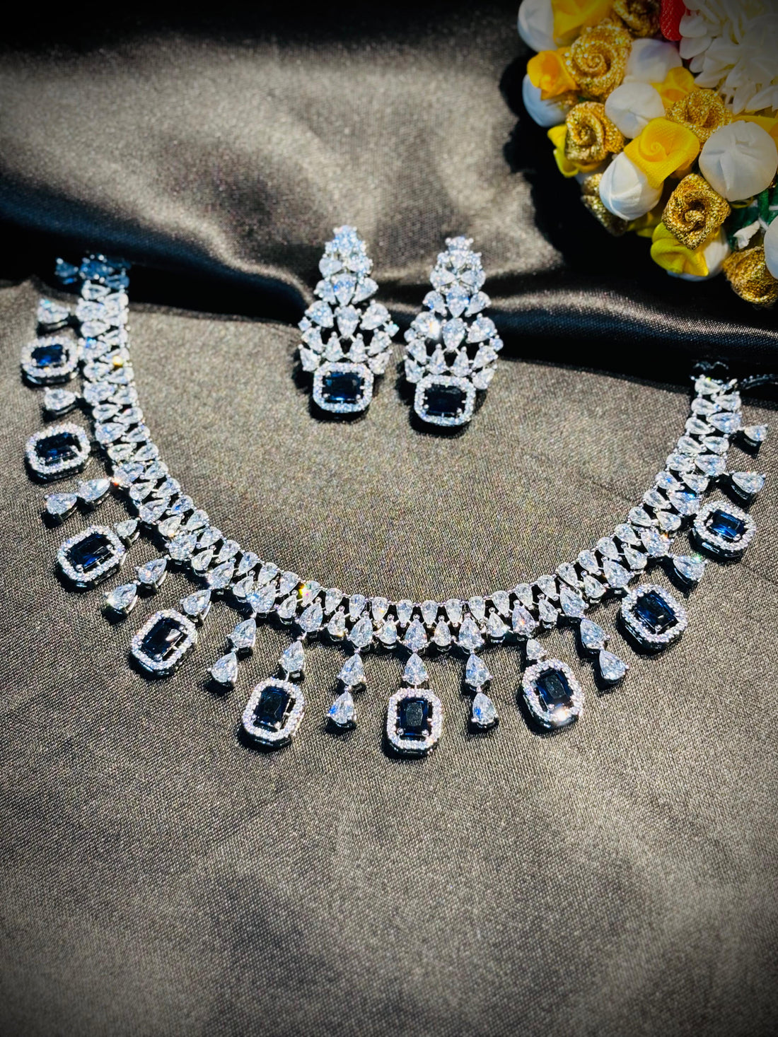 Diamond necklace and earrings on a dark fabric background with flowers.