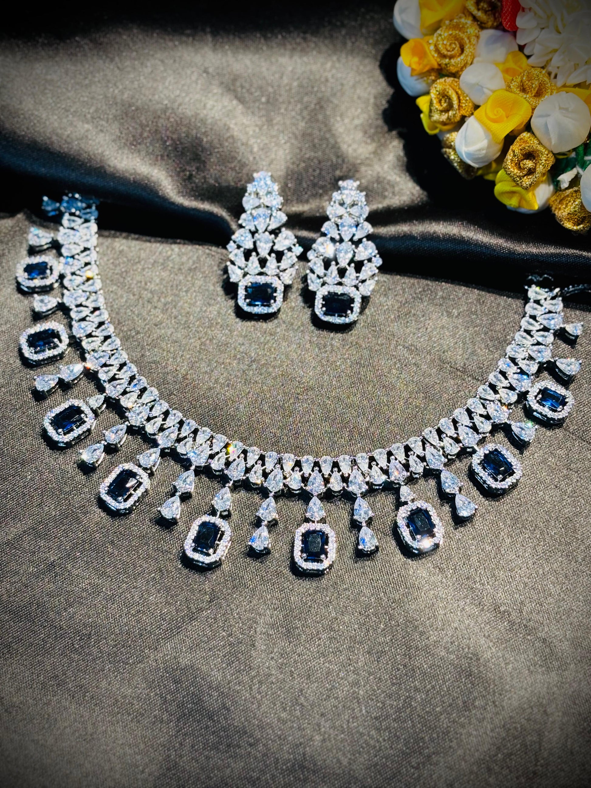 Diamond necklace and earrings on a dark fabric background with flowers.