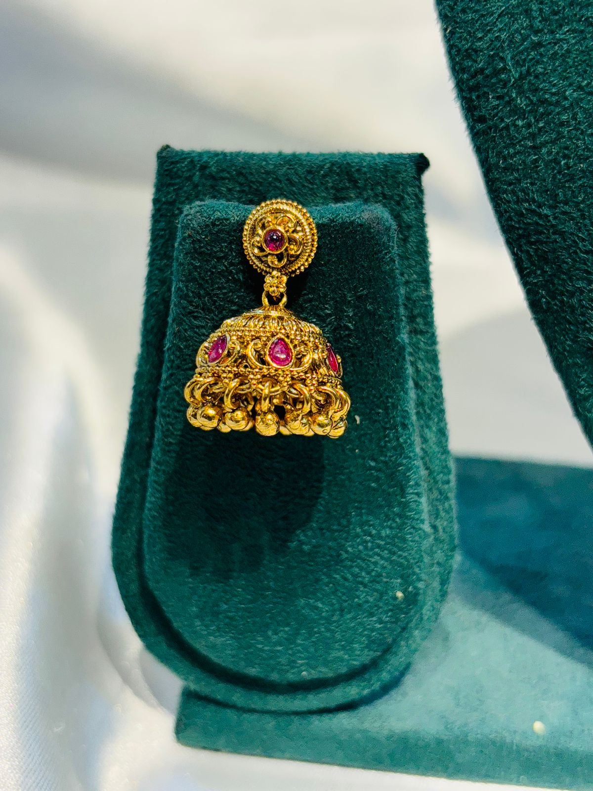 Gold earring with red gemstones on a green velvet stand