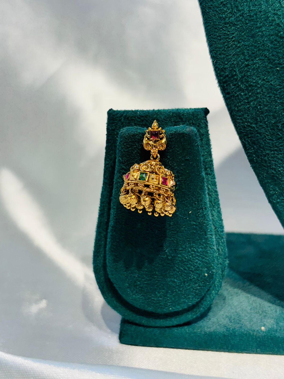 Gold earring with gemstones on a green velvet stand