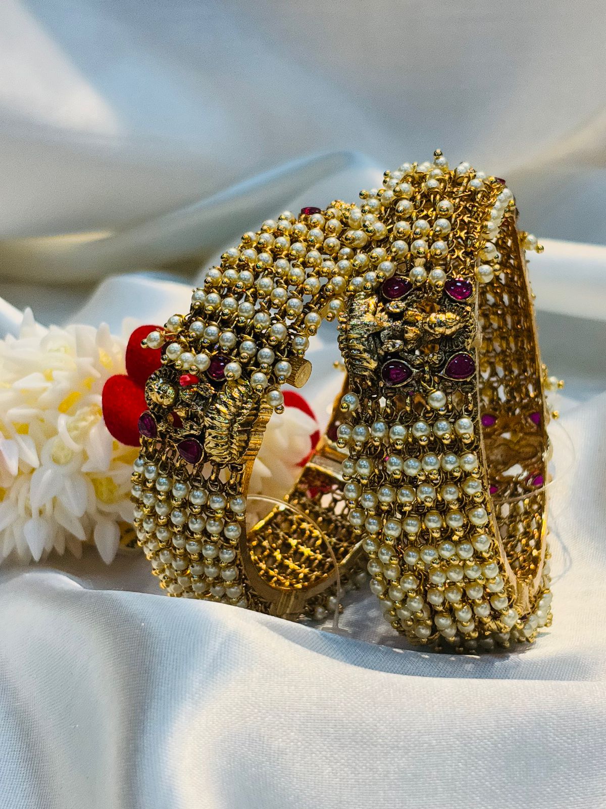 Gold bracelet with pearls and red stones on a white fabric background