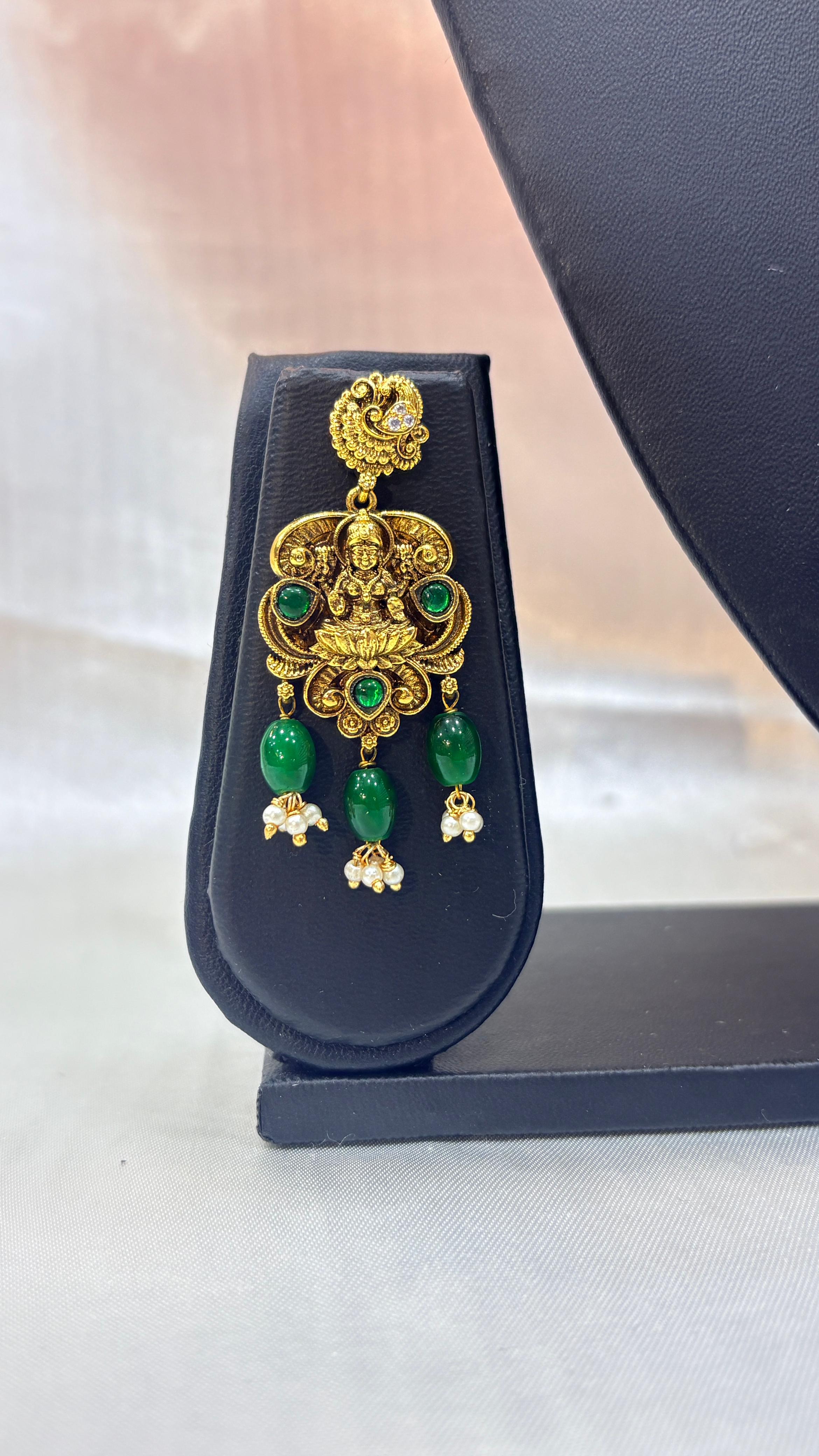 Gold and green gemstone earring on a black stand