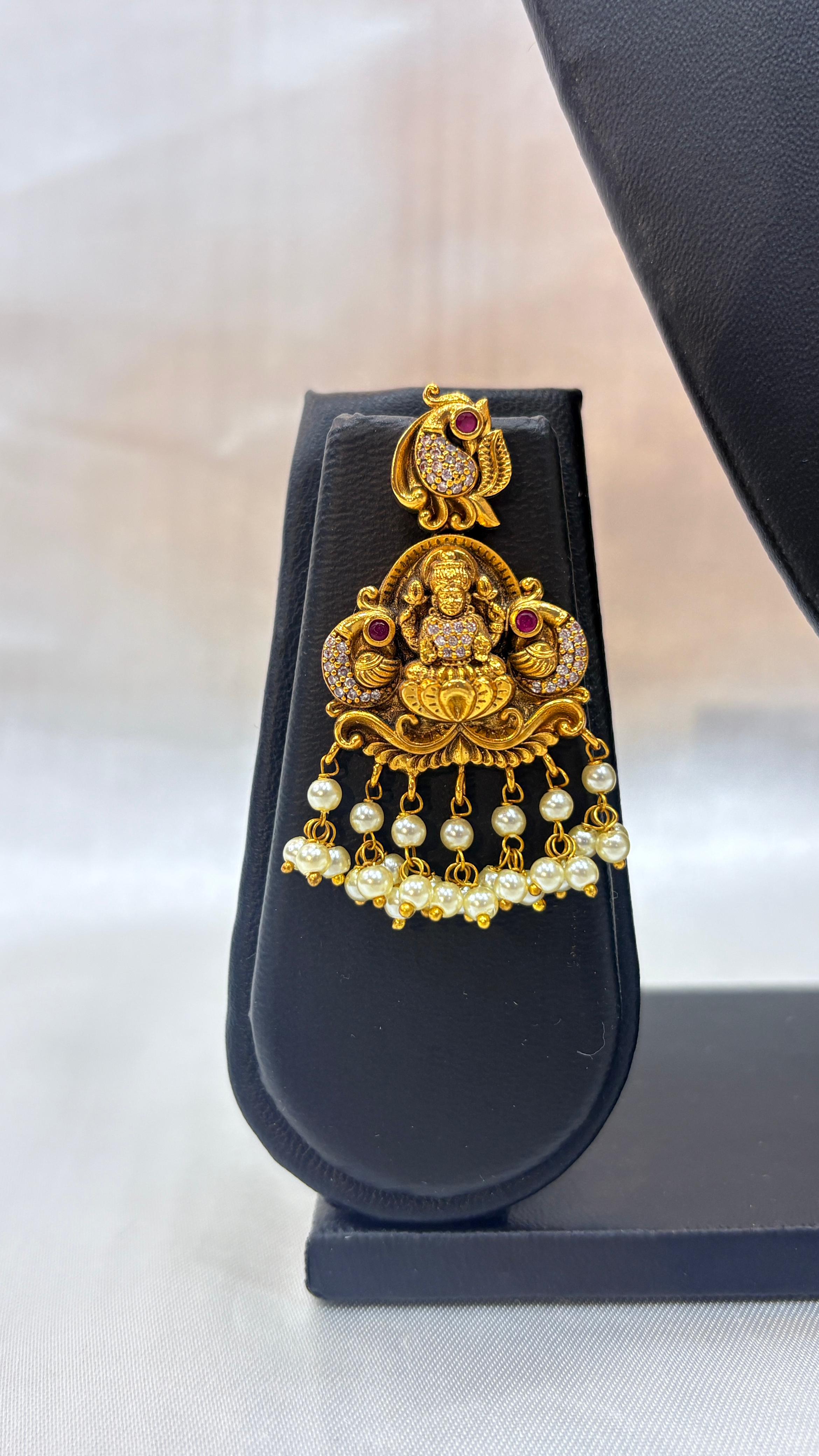 Gold and pearl earring on a black stand with a white background