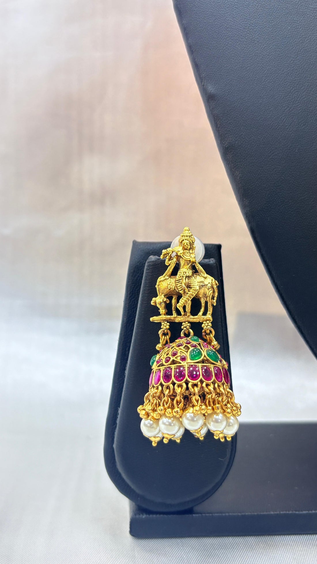 Gold necklace with pendant and matching earrings on a black stand against a white background