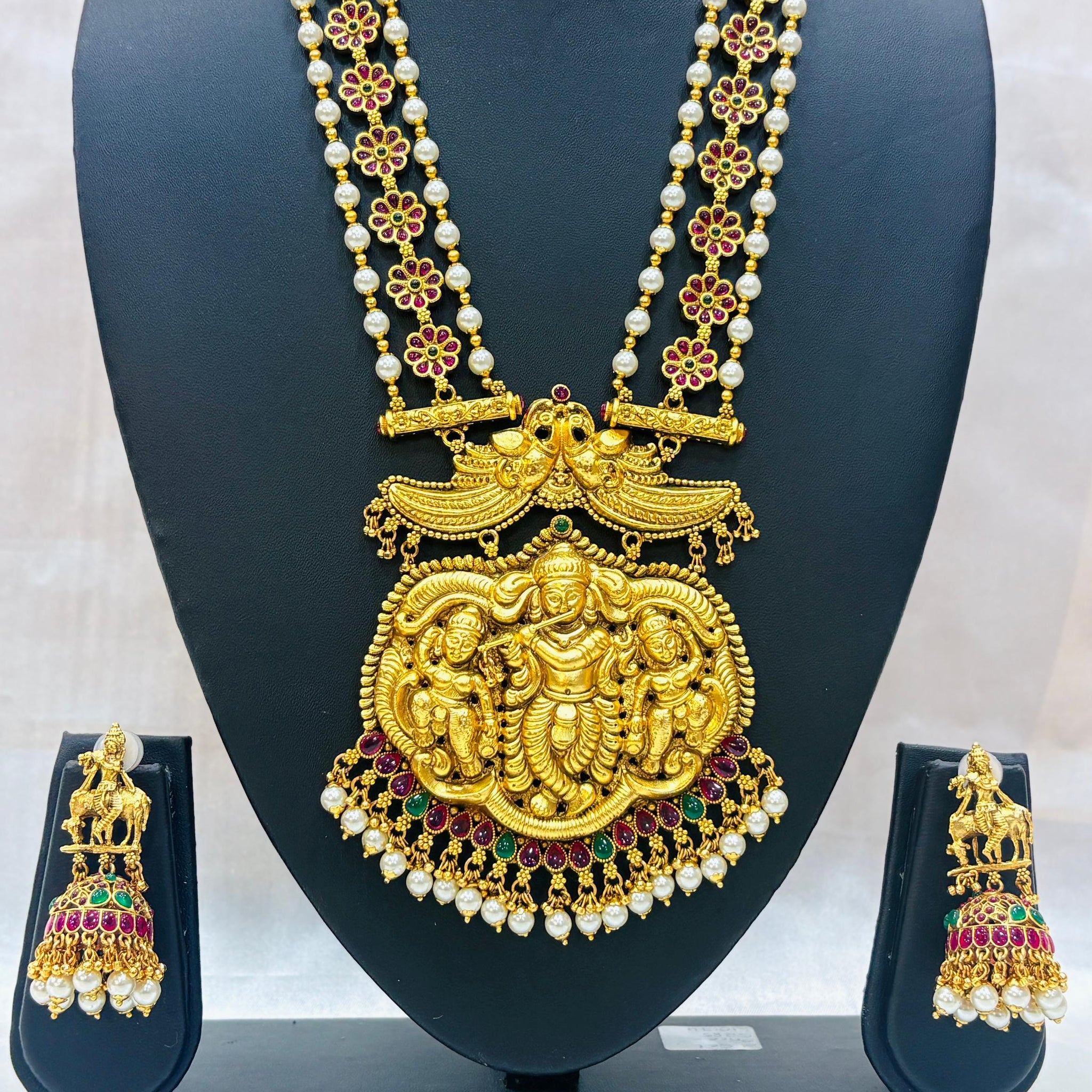Gold necklace with pendant and matching earrings on a black stand against a white background