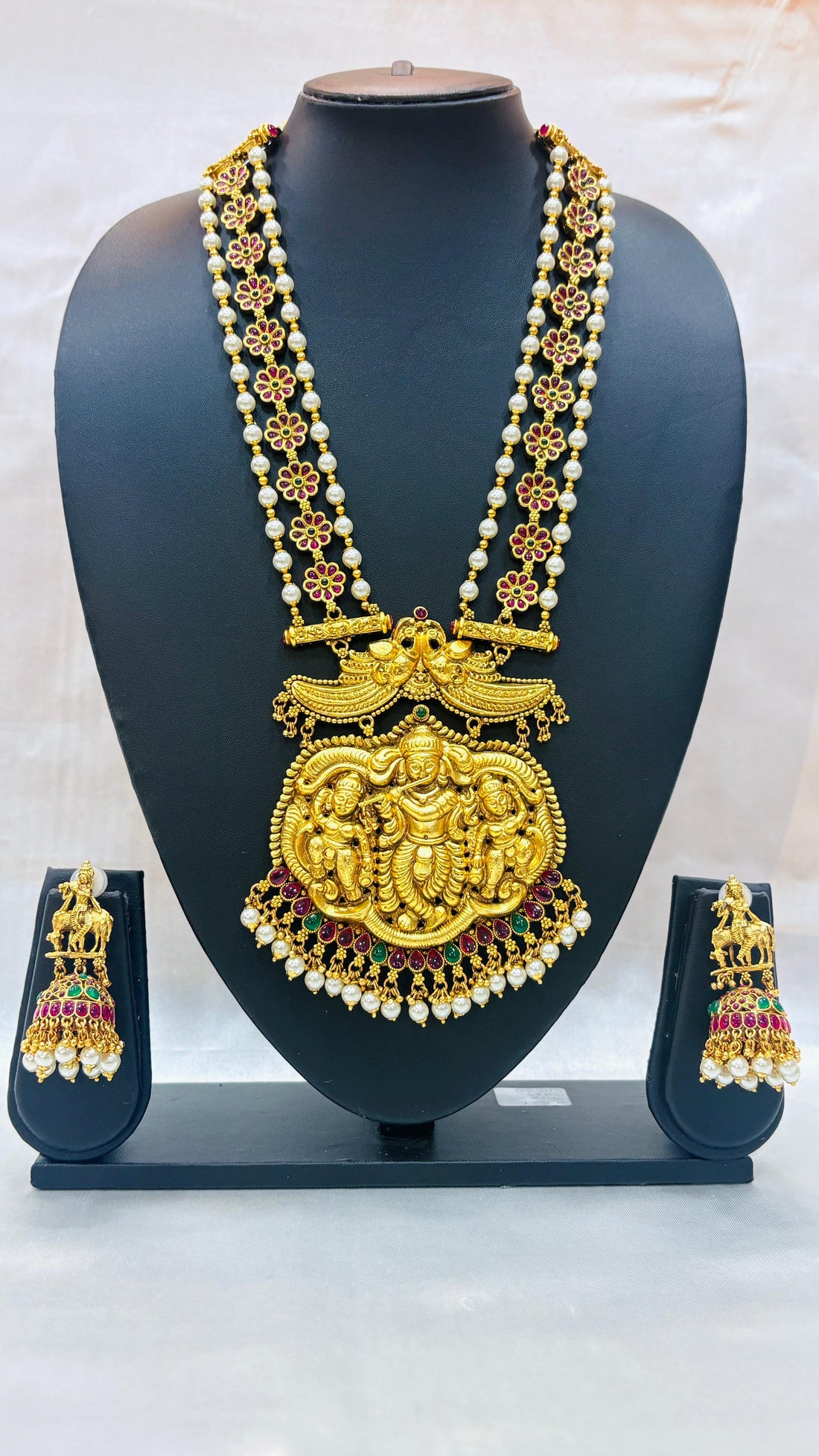 Gold necklace with pendant and matching earrings on a black stand against a white background