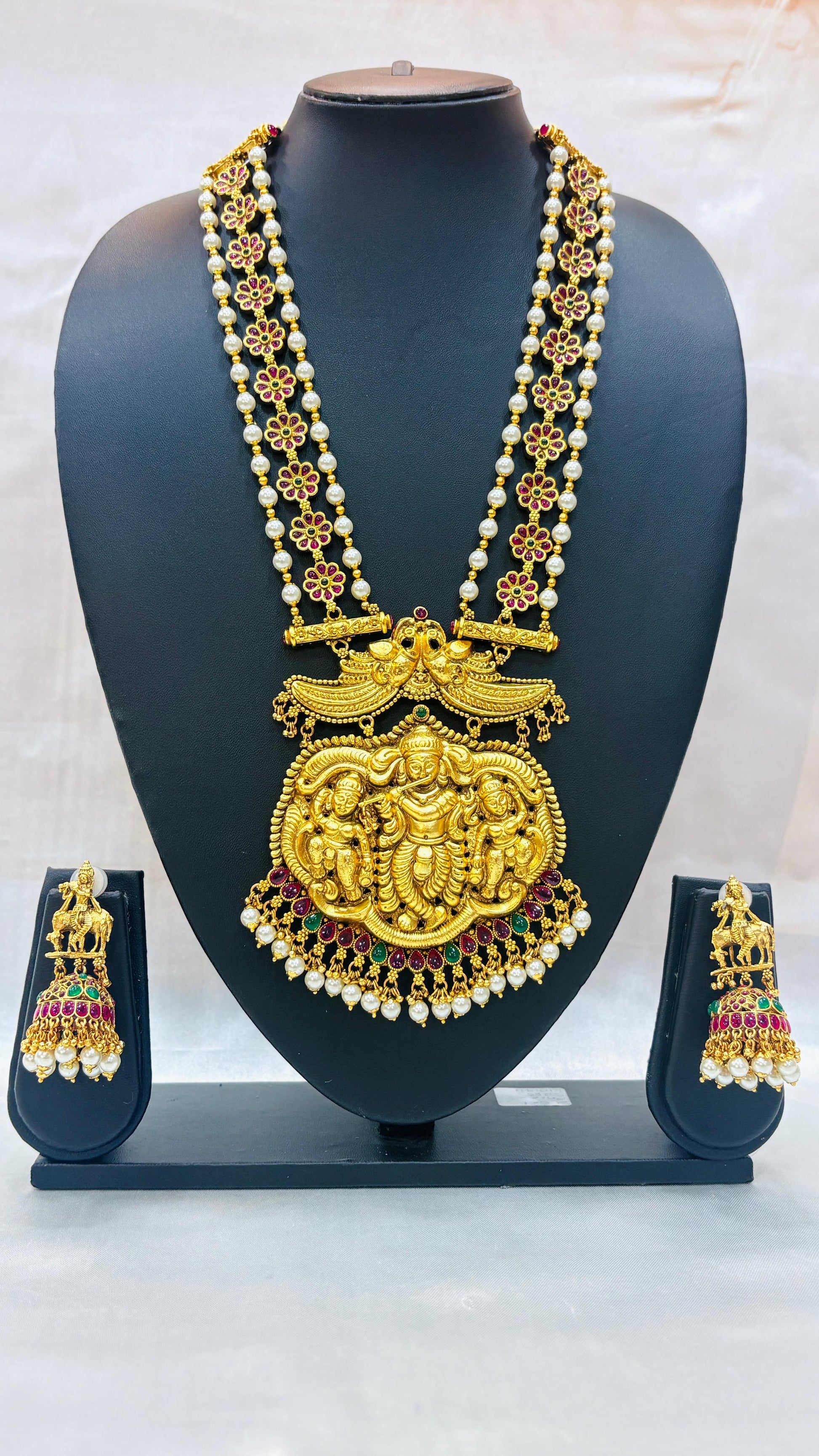 Gold necklace with pendant and matching earrings on a black stand against a white background