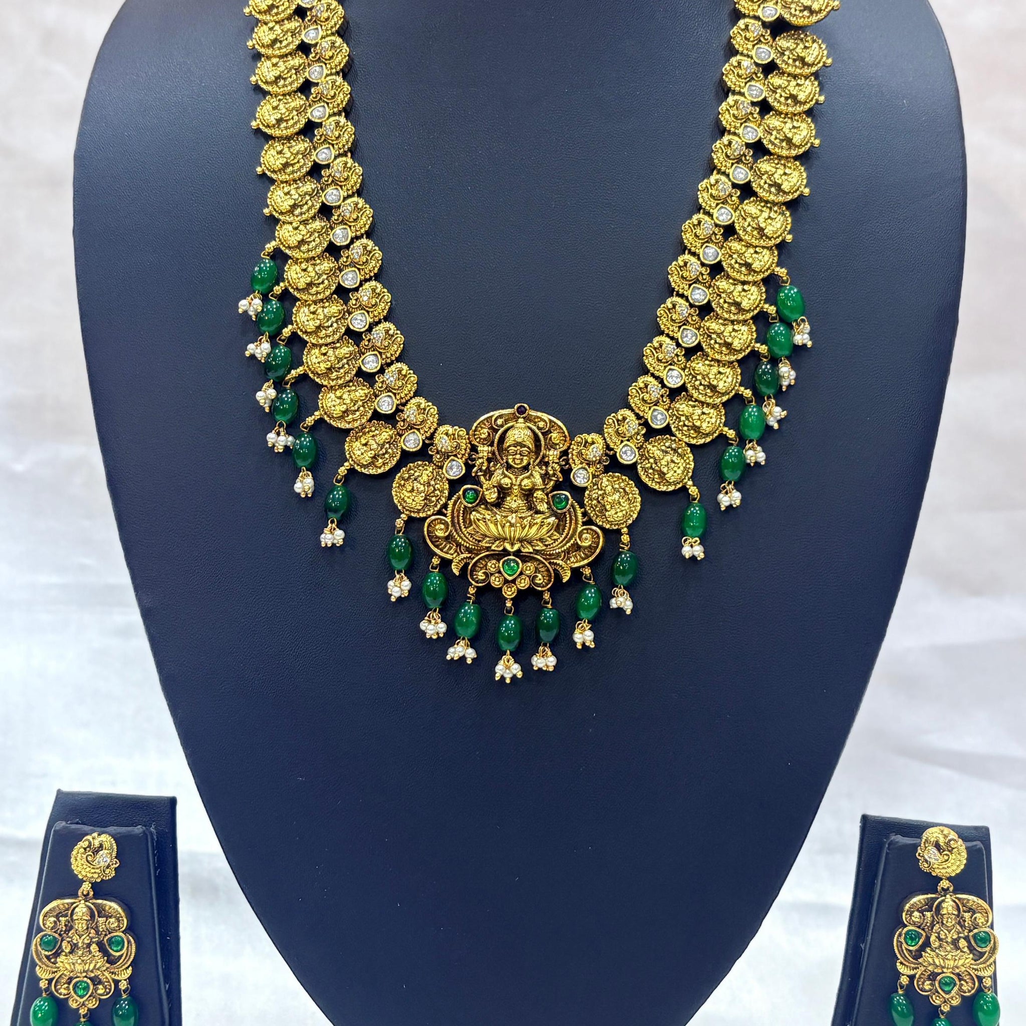 Gold necklace with green accents on a blue mannequin bust against a white background
