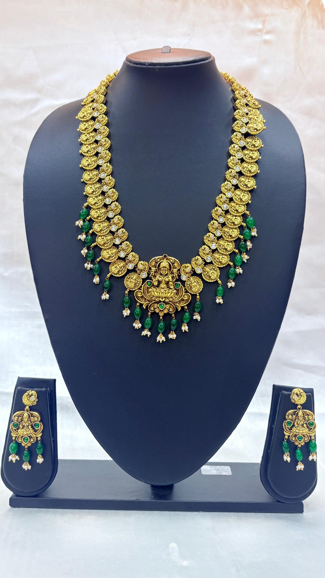 Gold necklace with green accents on a blue mannequin bust against a white background