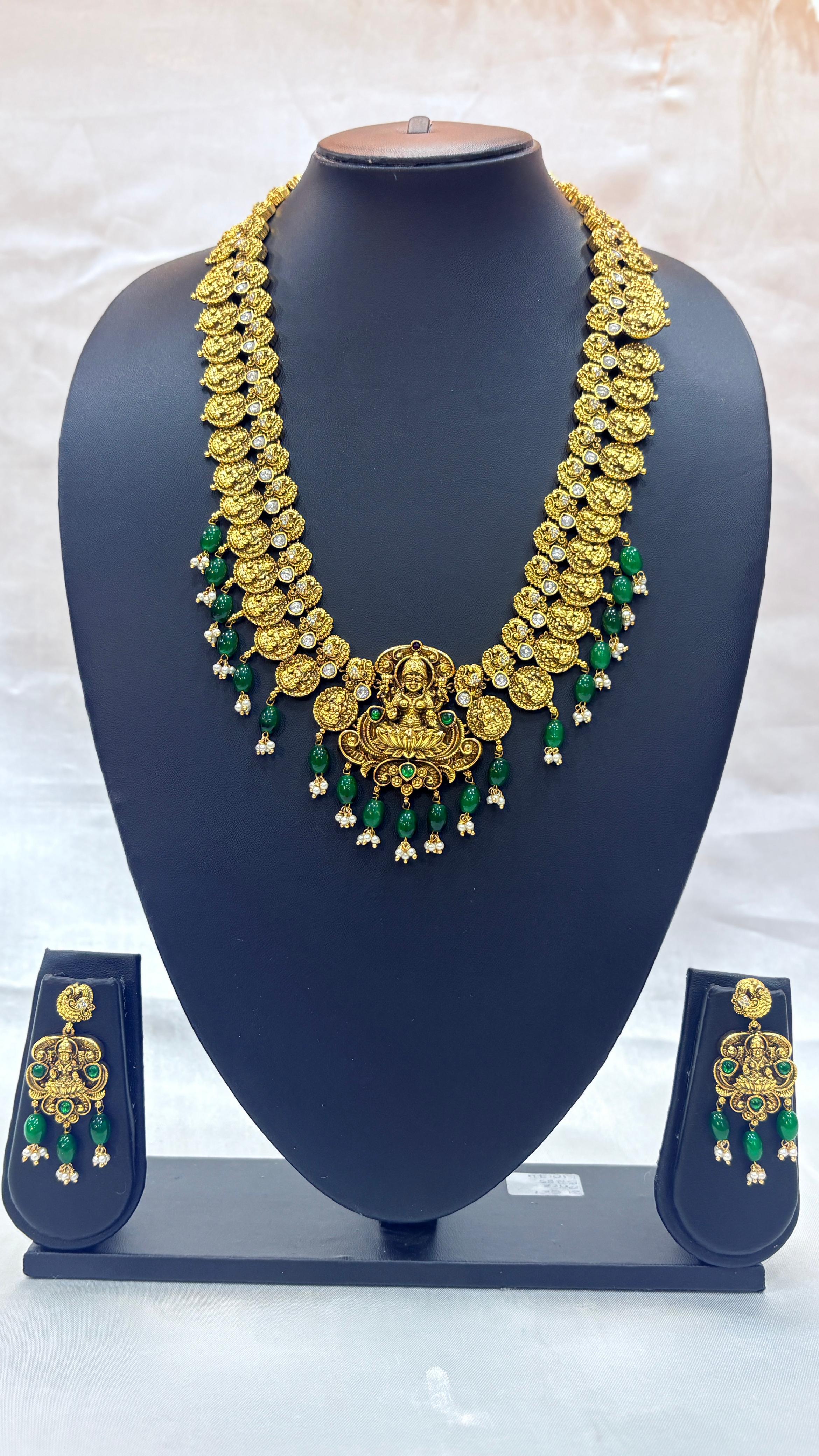 Gold necklace with green accents on a blue mannequin bust against a white background
