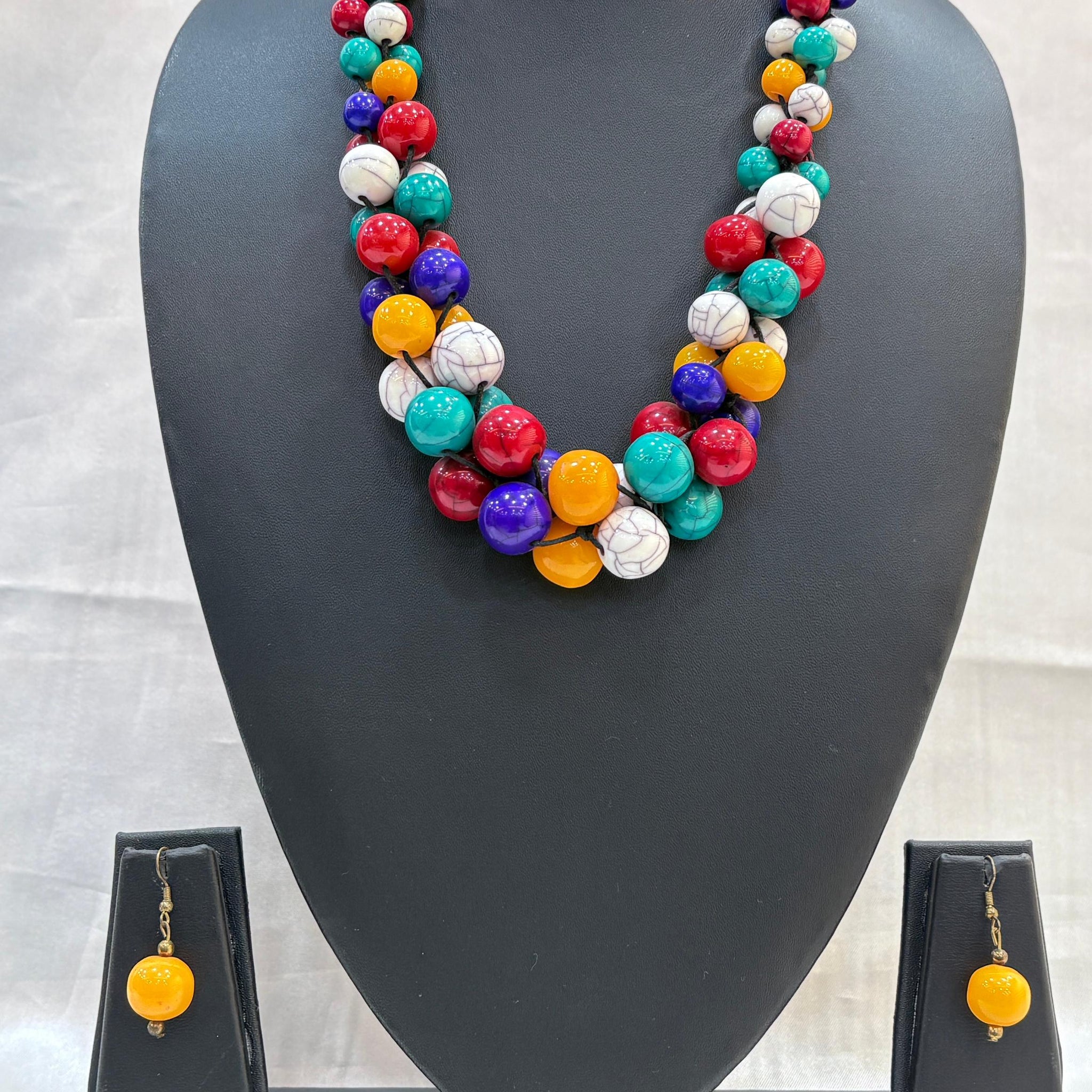 Colorful beaded necklace and earrings on a gray mannequin bust against a light background