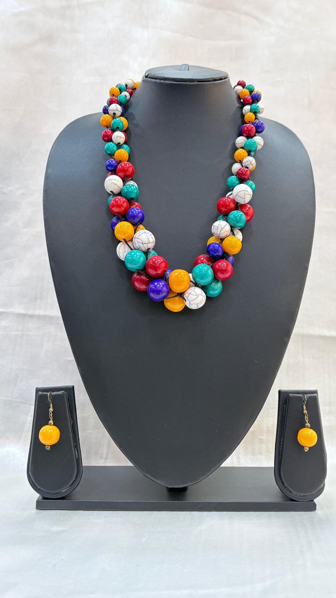Colorful beaded necklace and earrings on a gray mannequin bust against a light background