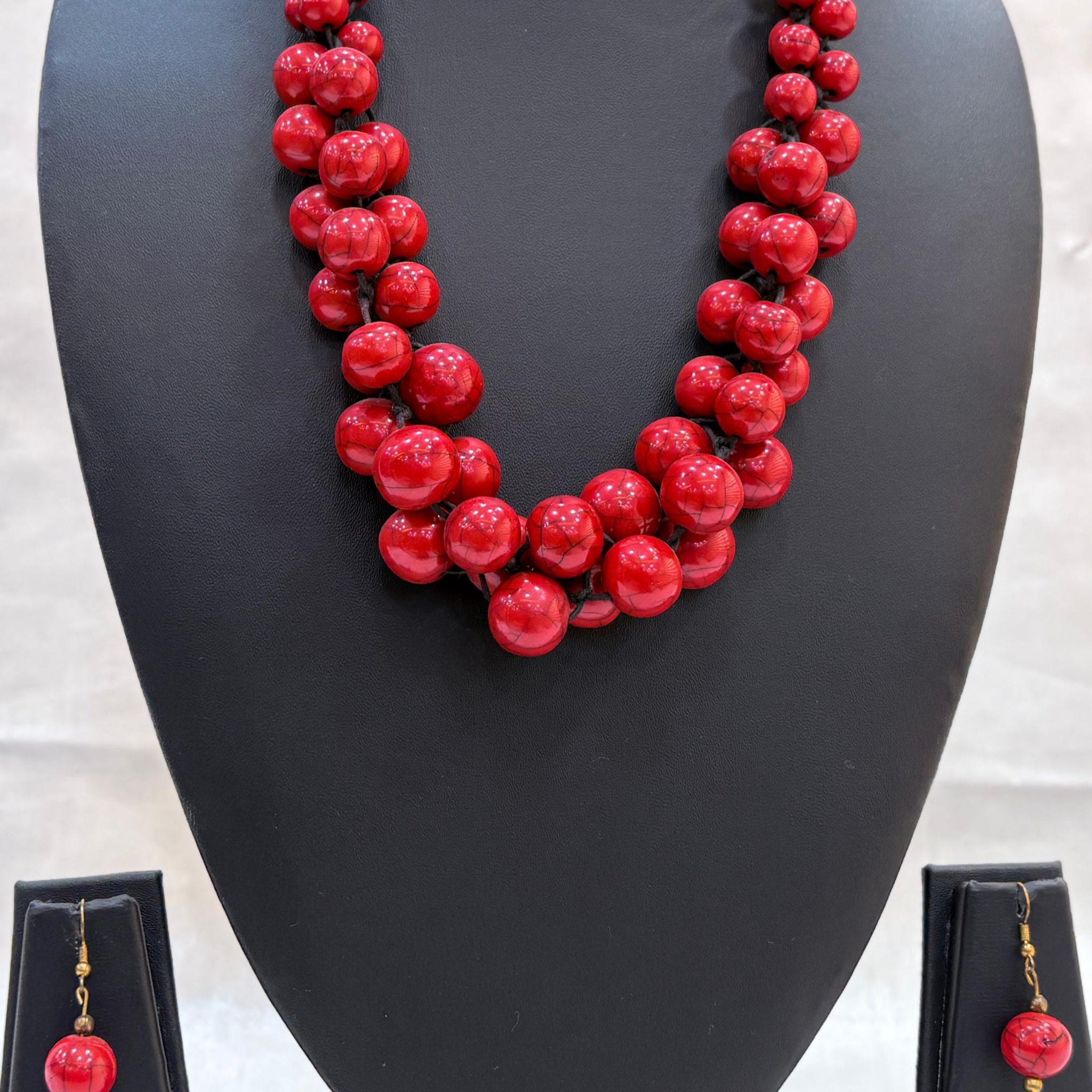 Red beaded necklace on a black mannequin bust with matching earrings below.