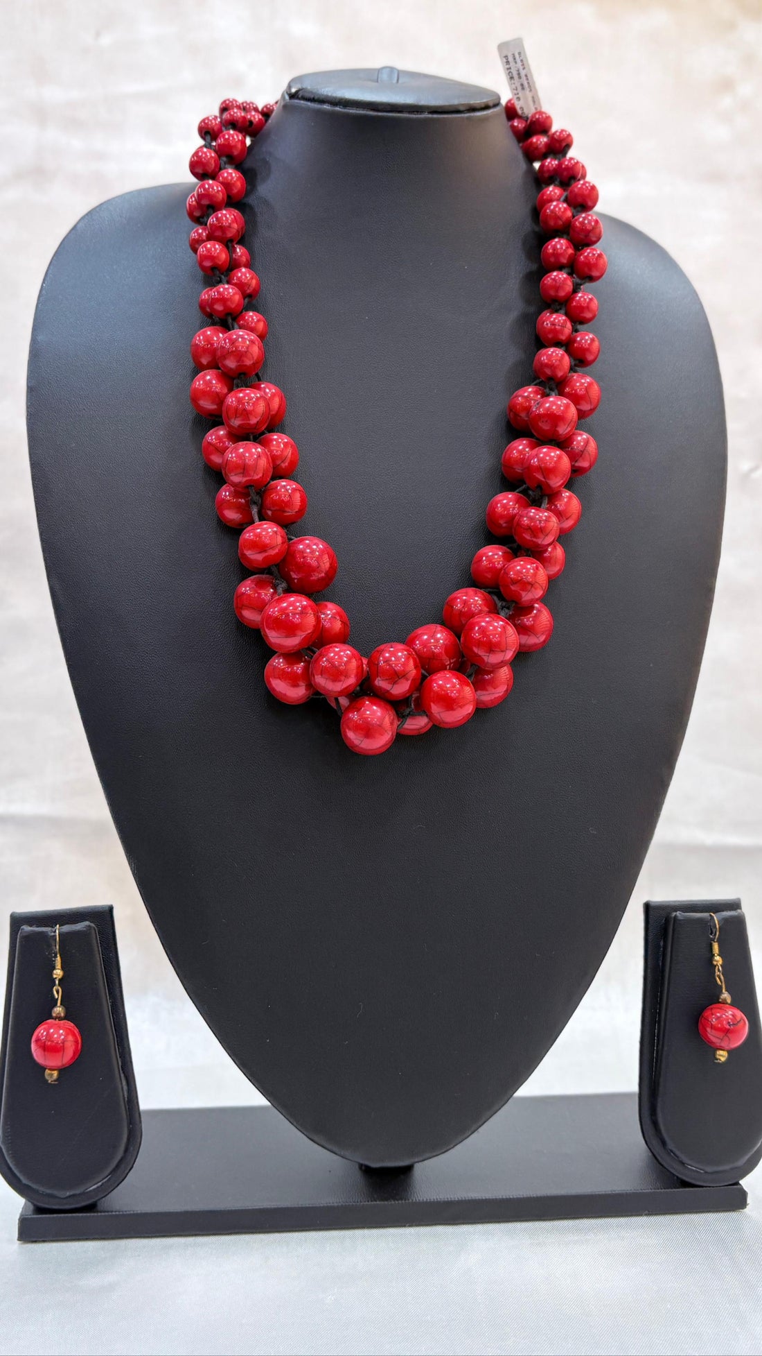 Red beaded necklace on a black mannequin bust with matching earrings below.