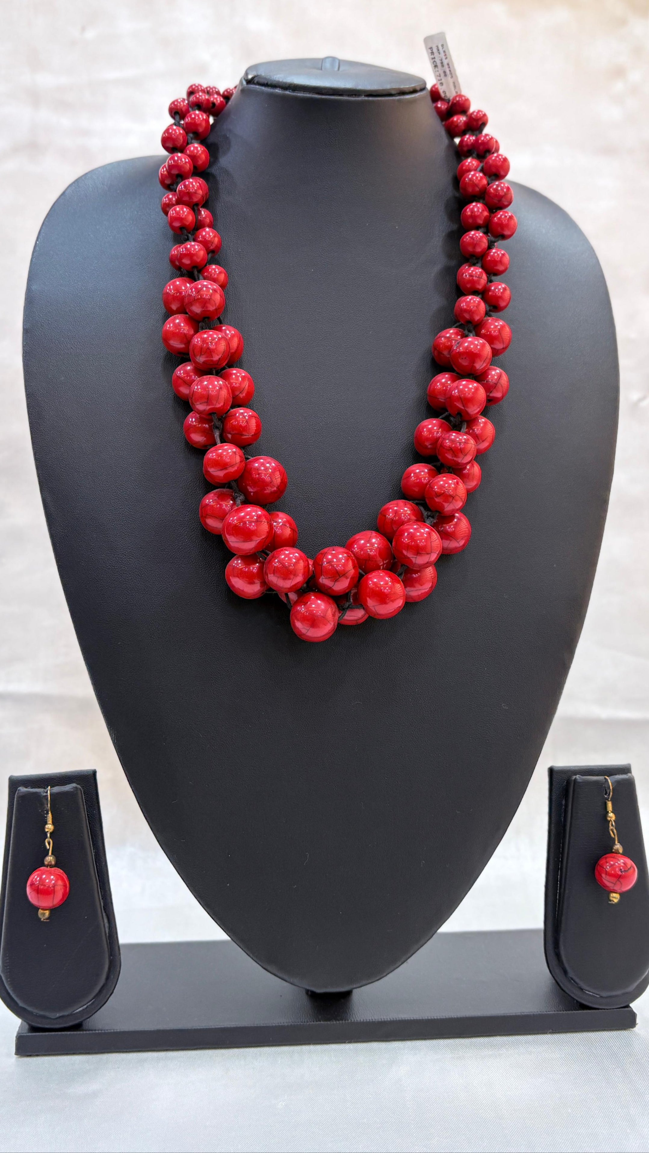 Red beaded necklace on a black mannequin bust with matching earrings below.
