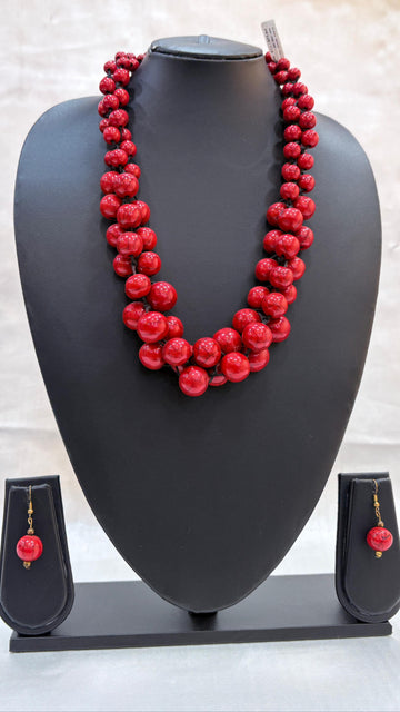 Red beaded necklace on a black mannequin bust with matching earrings below.
