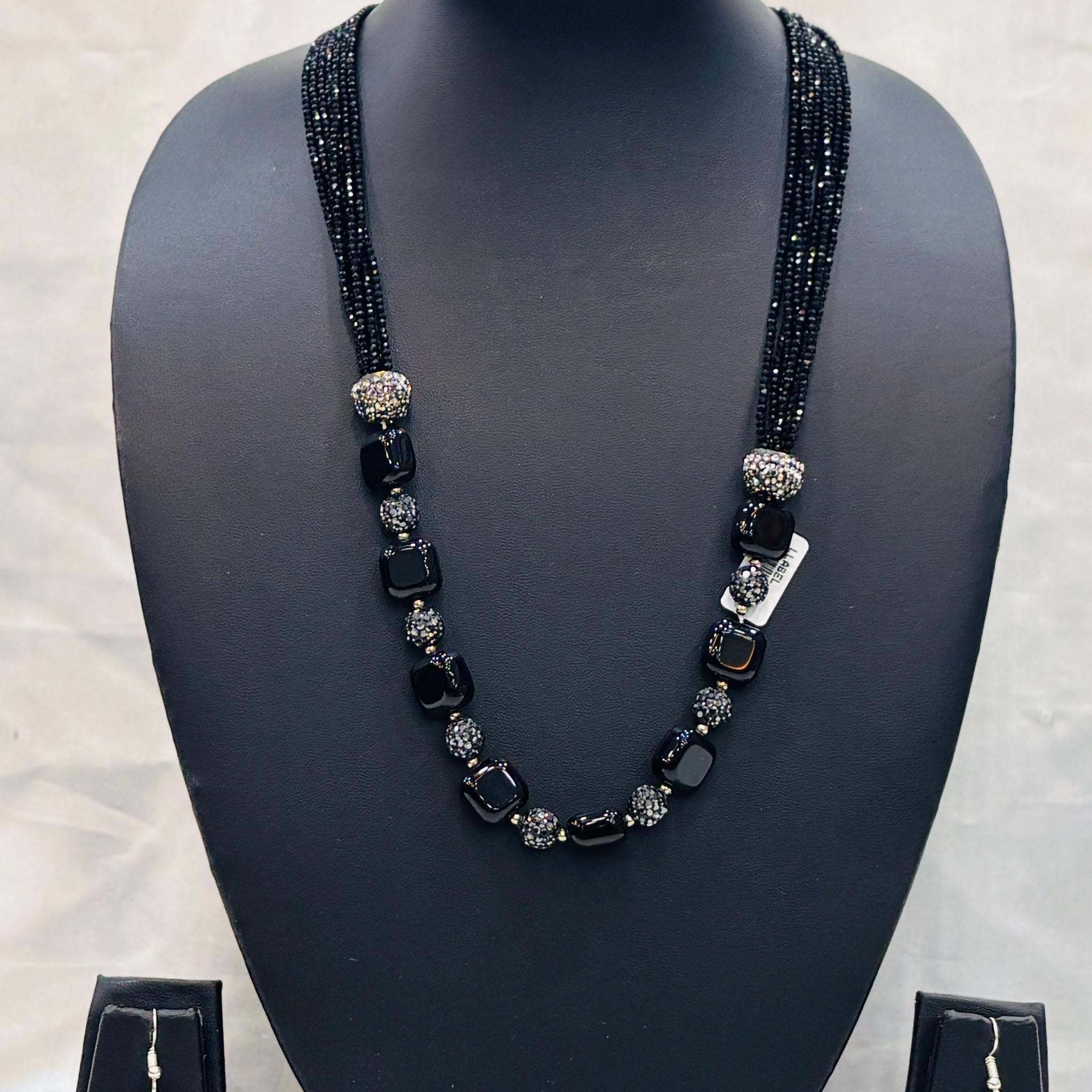 Black beaded necklace and earrings set on a black mannequin bust with a light gray background.