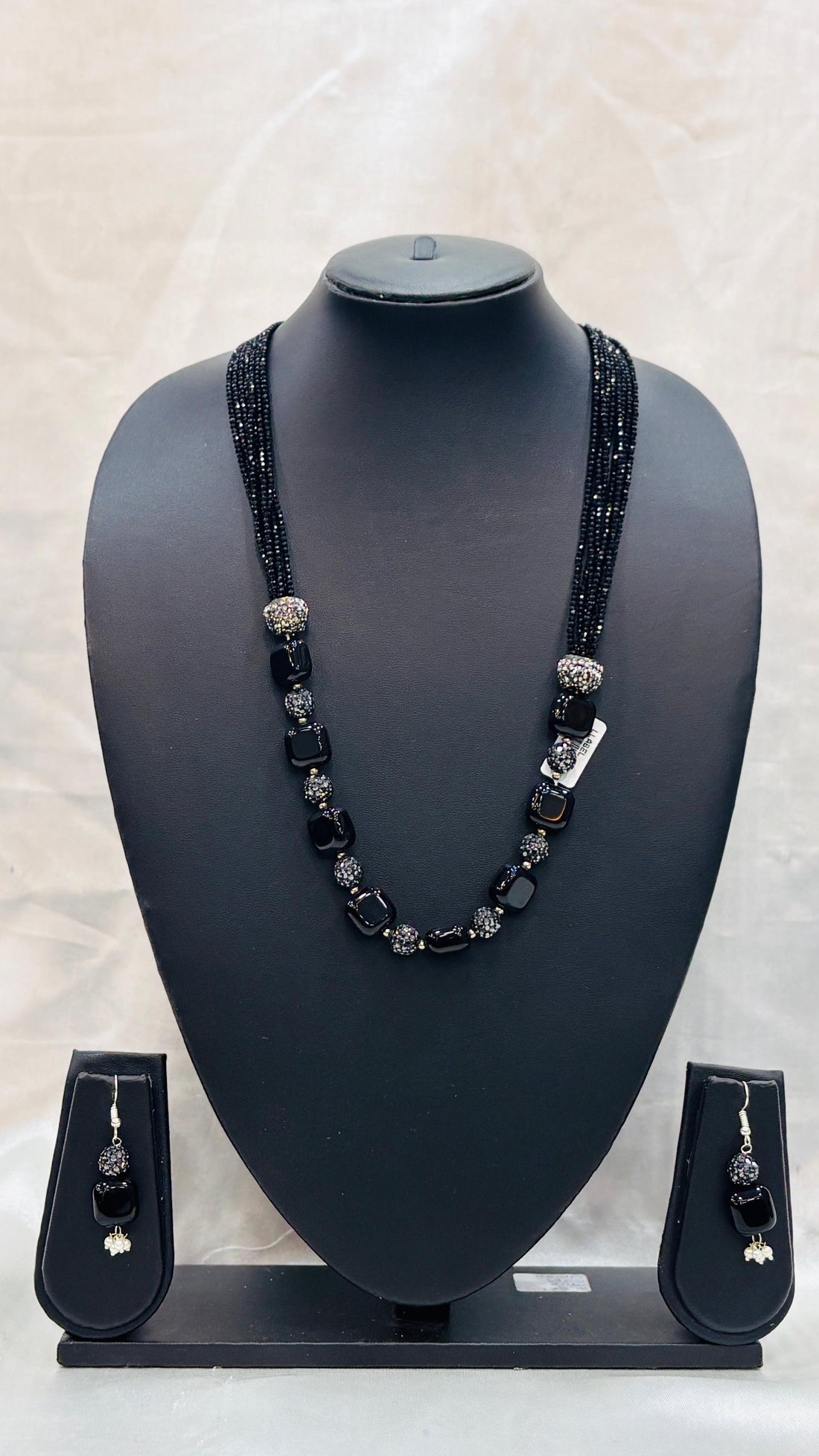 Black beaded necklace and earrings set on a black mannequin bust with a light gray background.