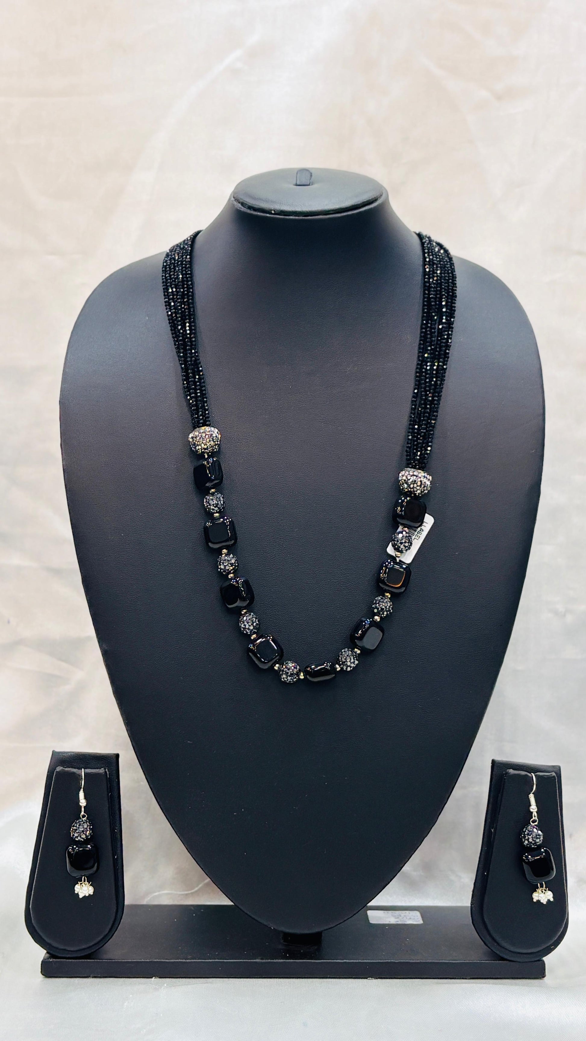 Black beaded necklace and earrings set on a black mannequin bust with a light gray background.