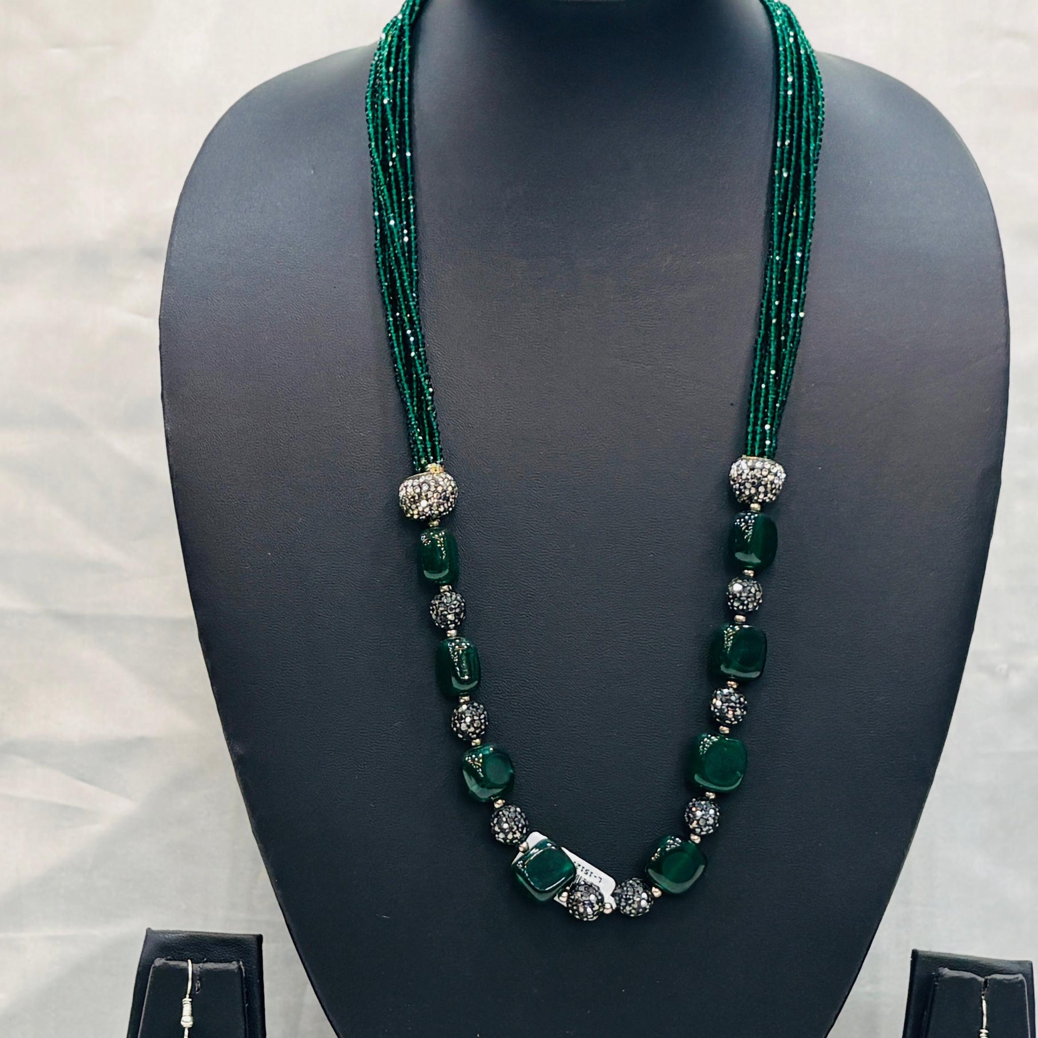 Green beaded necklace with matching earrings on a black mannequin bust against a white background