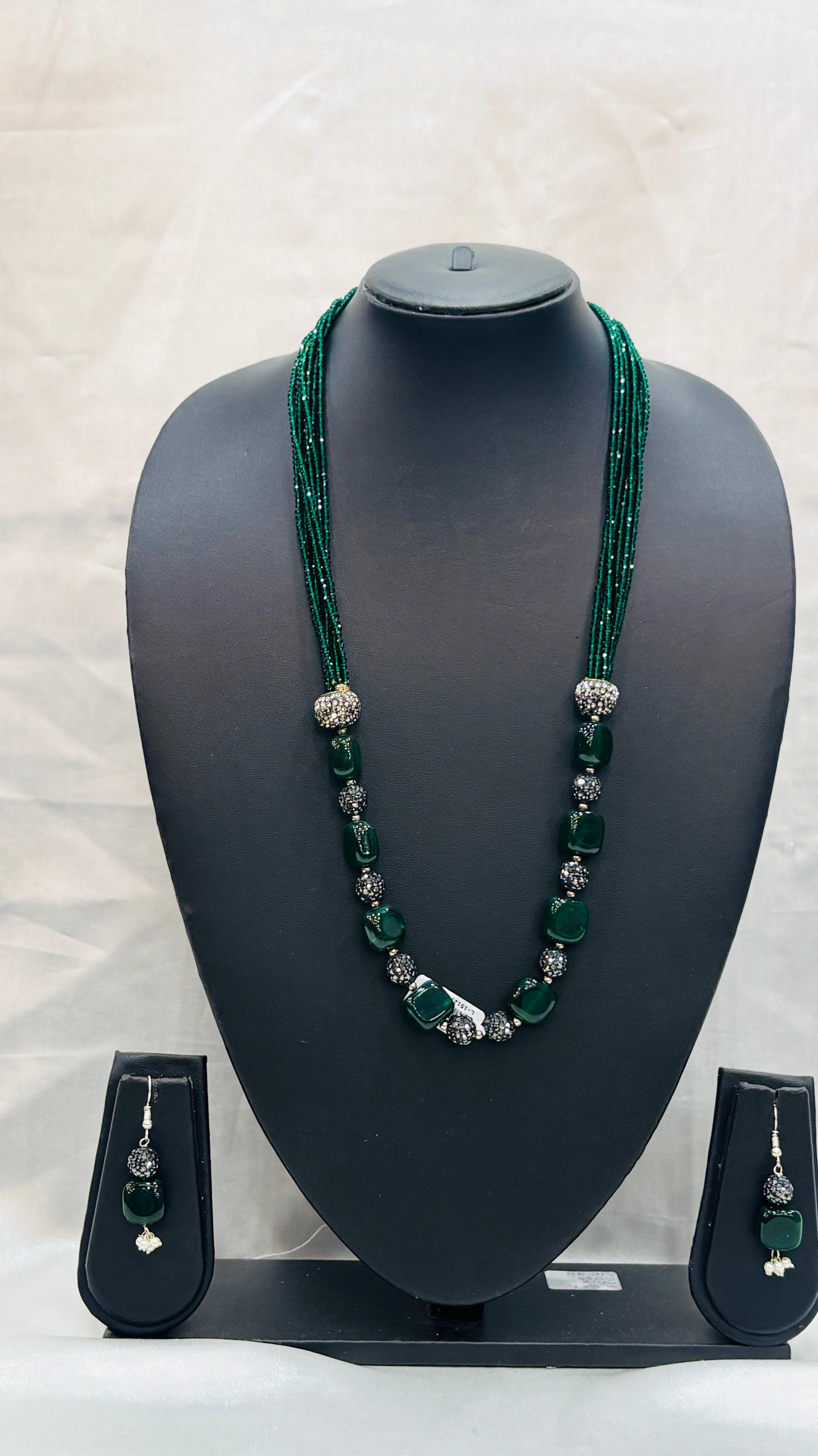 Green beaded necklace with matching earrings on a black mannequin bust against a white background