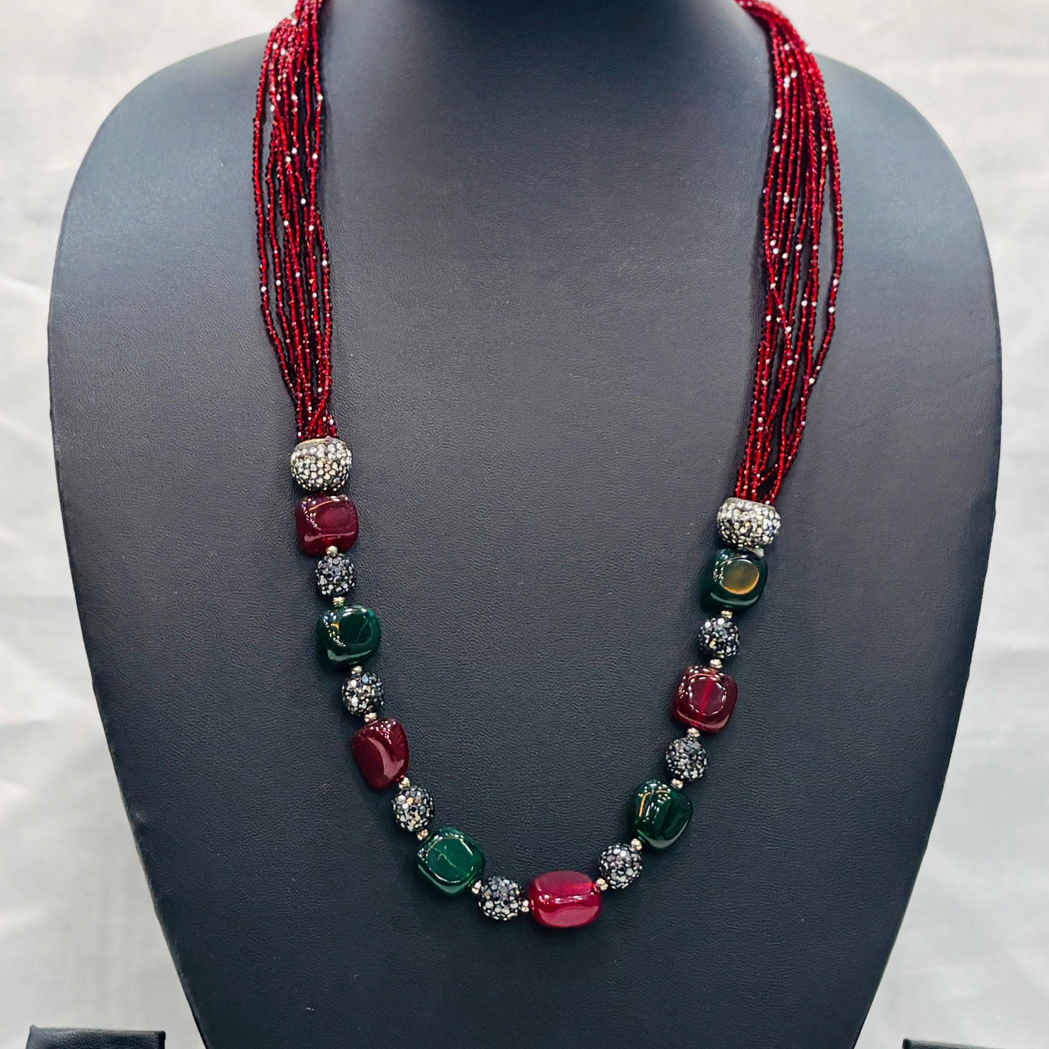 Necklace with red and green beads on a mannequin bust with matching earrings.