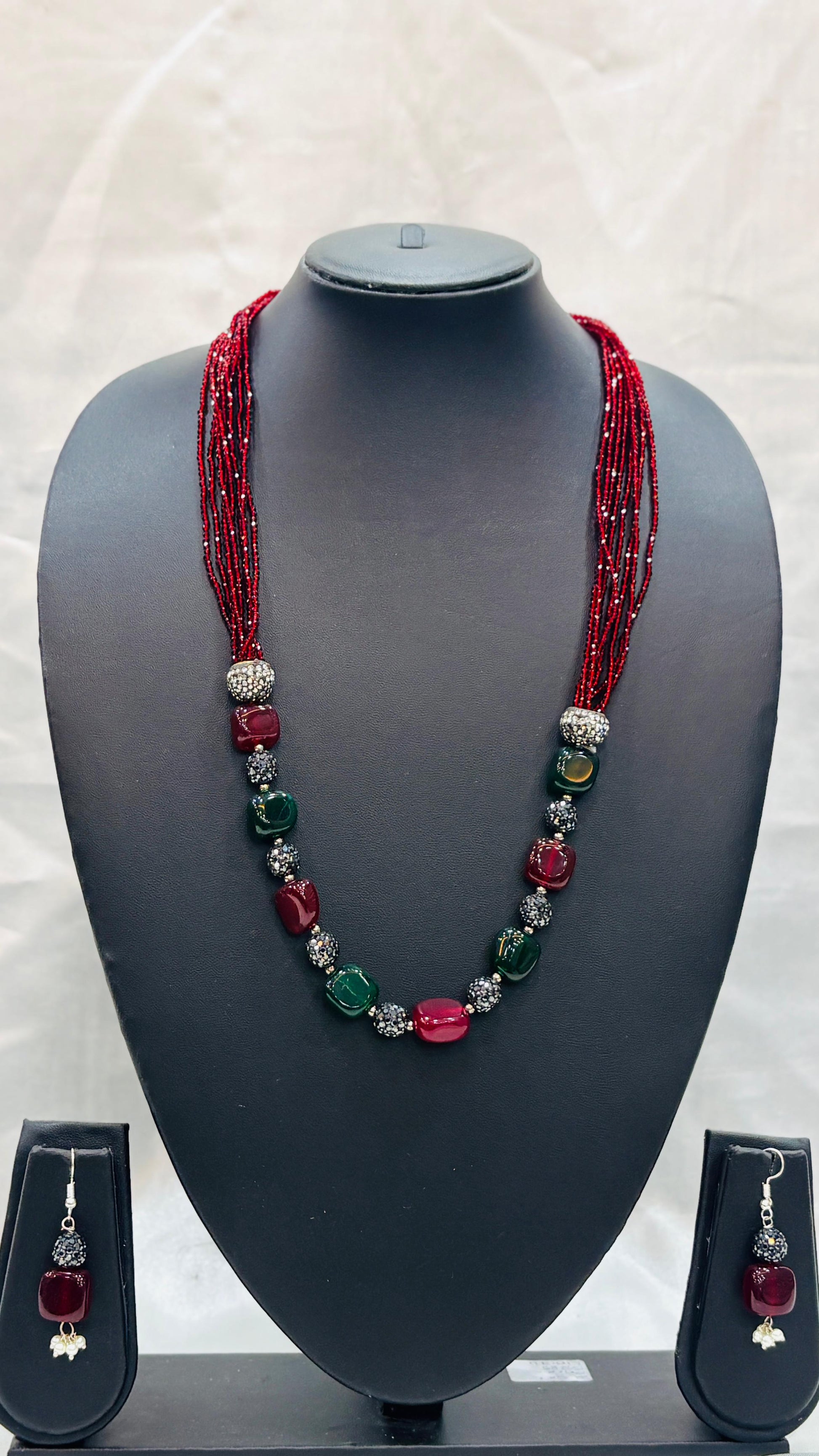 Necklace with red and green beads on a mannequin bust with matching earrings.